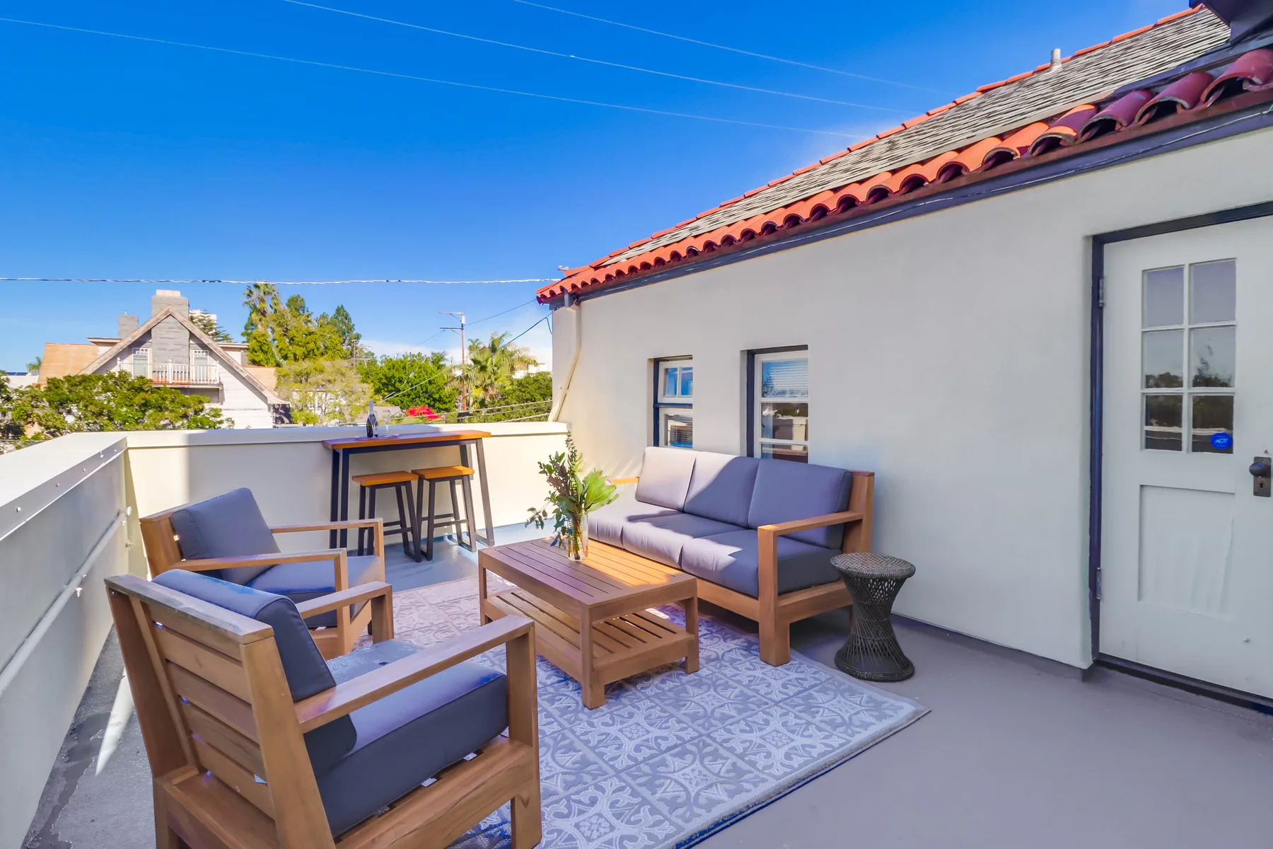 A rooftop terrace has cushioned seating and a small table beside the building.