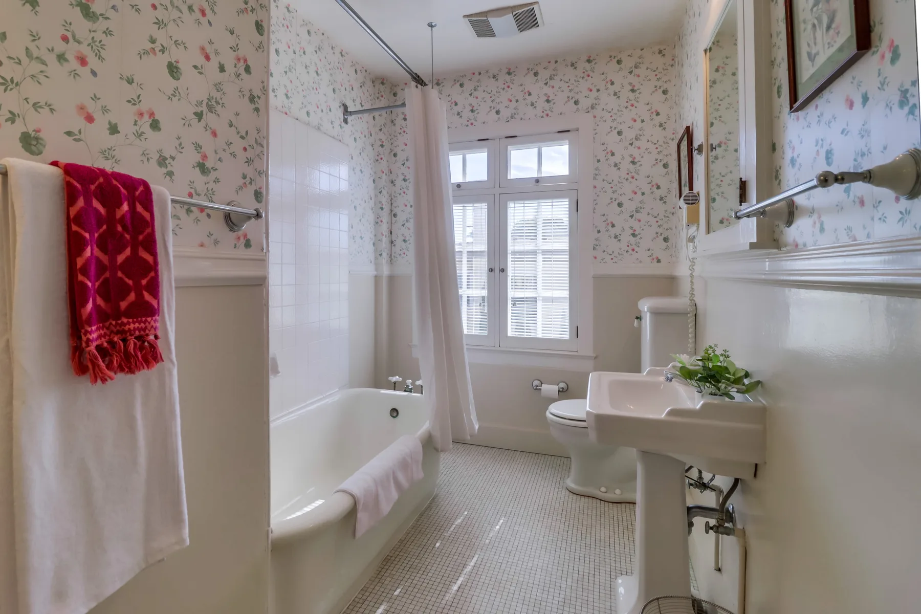 A bathroom with a bathtub, sink, and floral wallpaper.