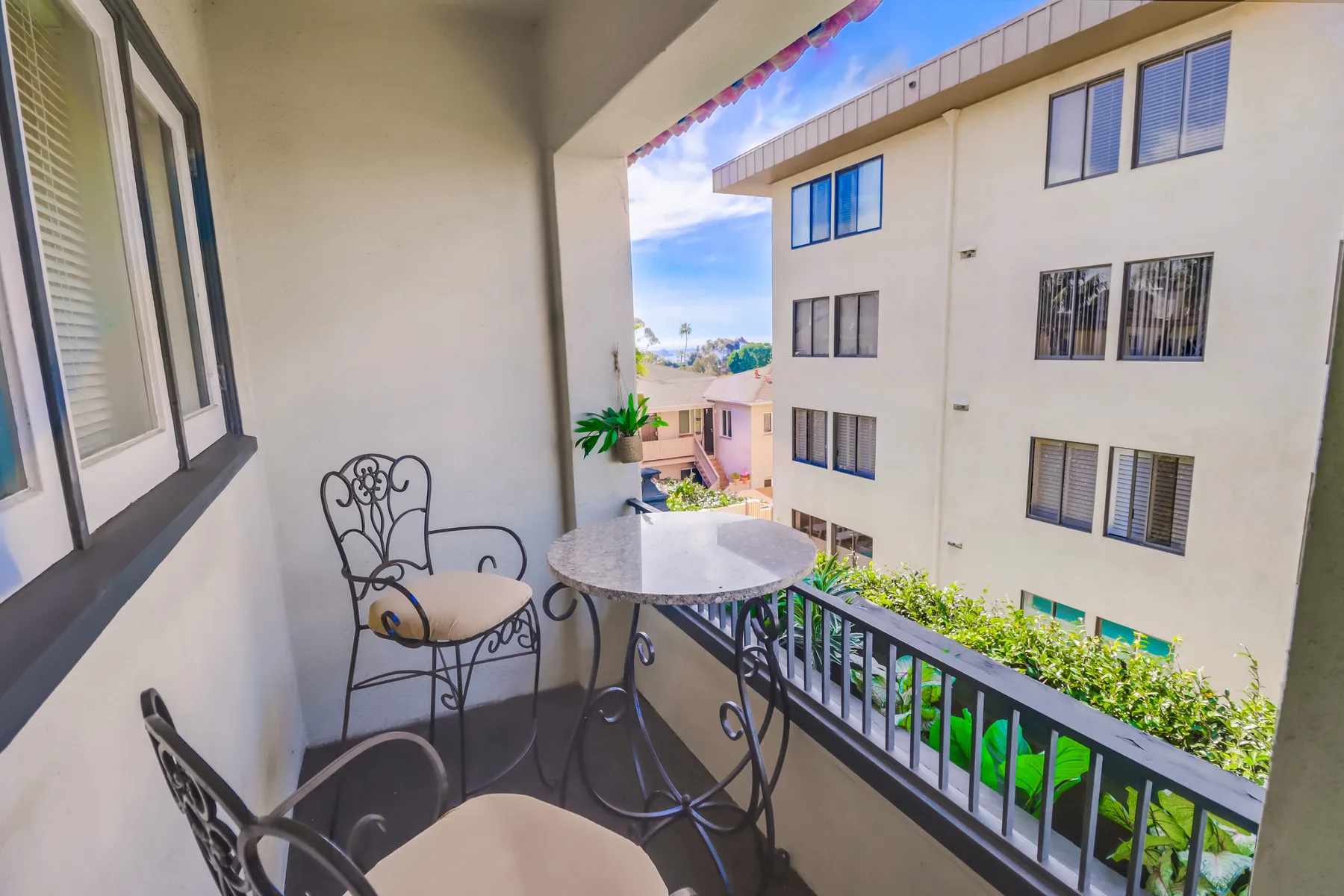 A small balcony has metal seating and a round table overlooking a neighboring building.