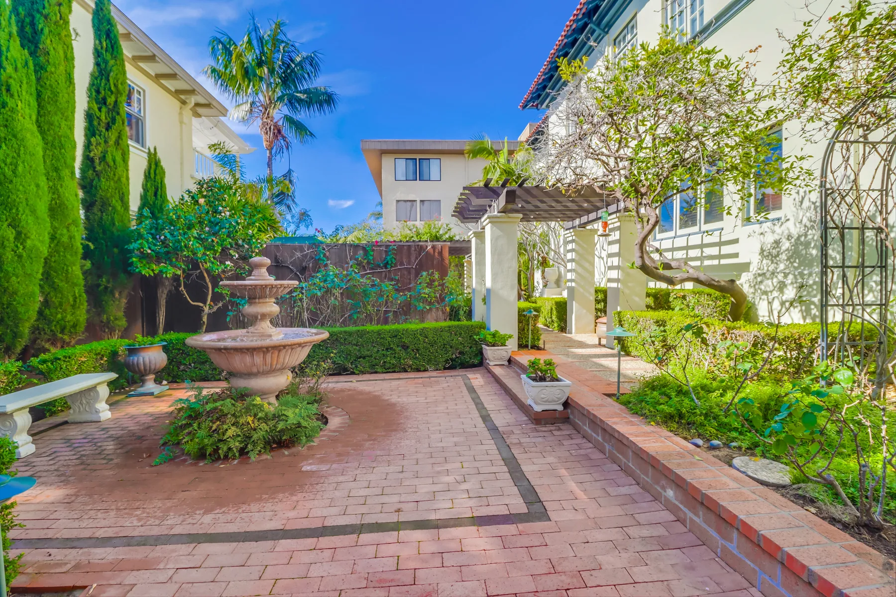 A landscaped courtyard with a paved walkway, fountain, and surrounding greenery.
