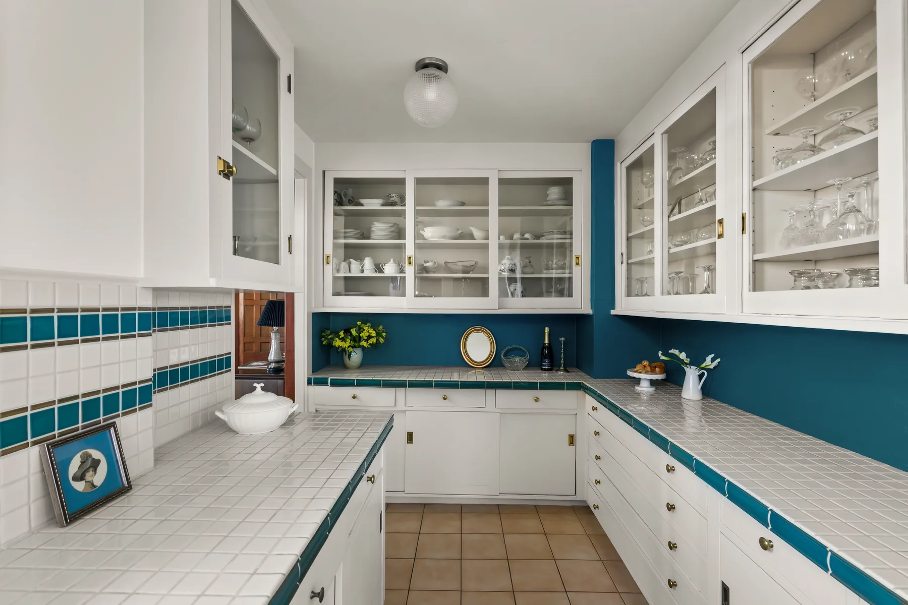 A bright kitchen with white cabinets, tiled counters, and teal accents.
