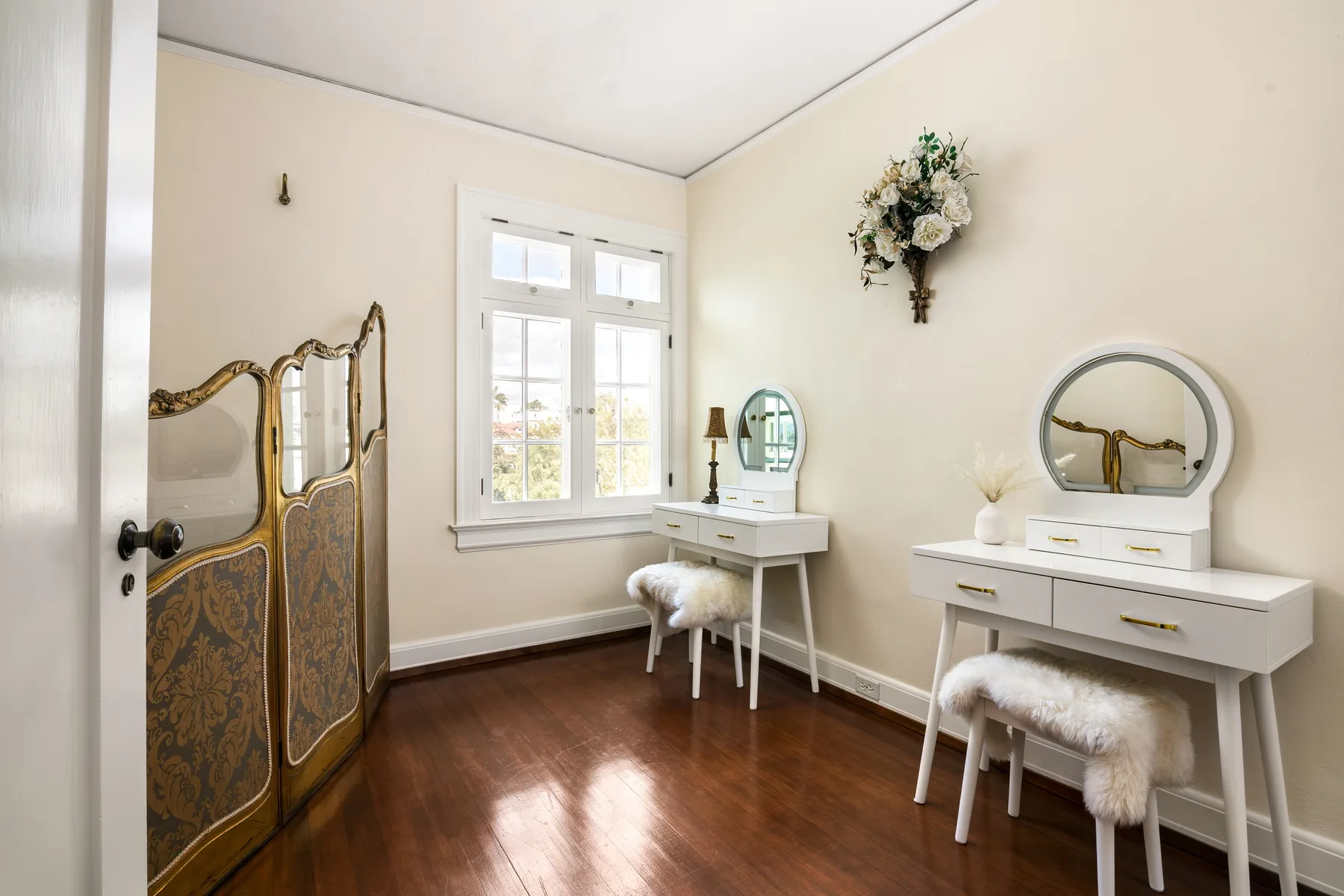 A dressing room with two white vanity tables and a decorative folding screen.