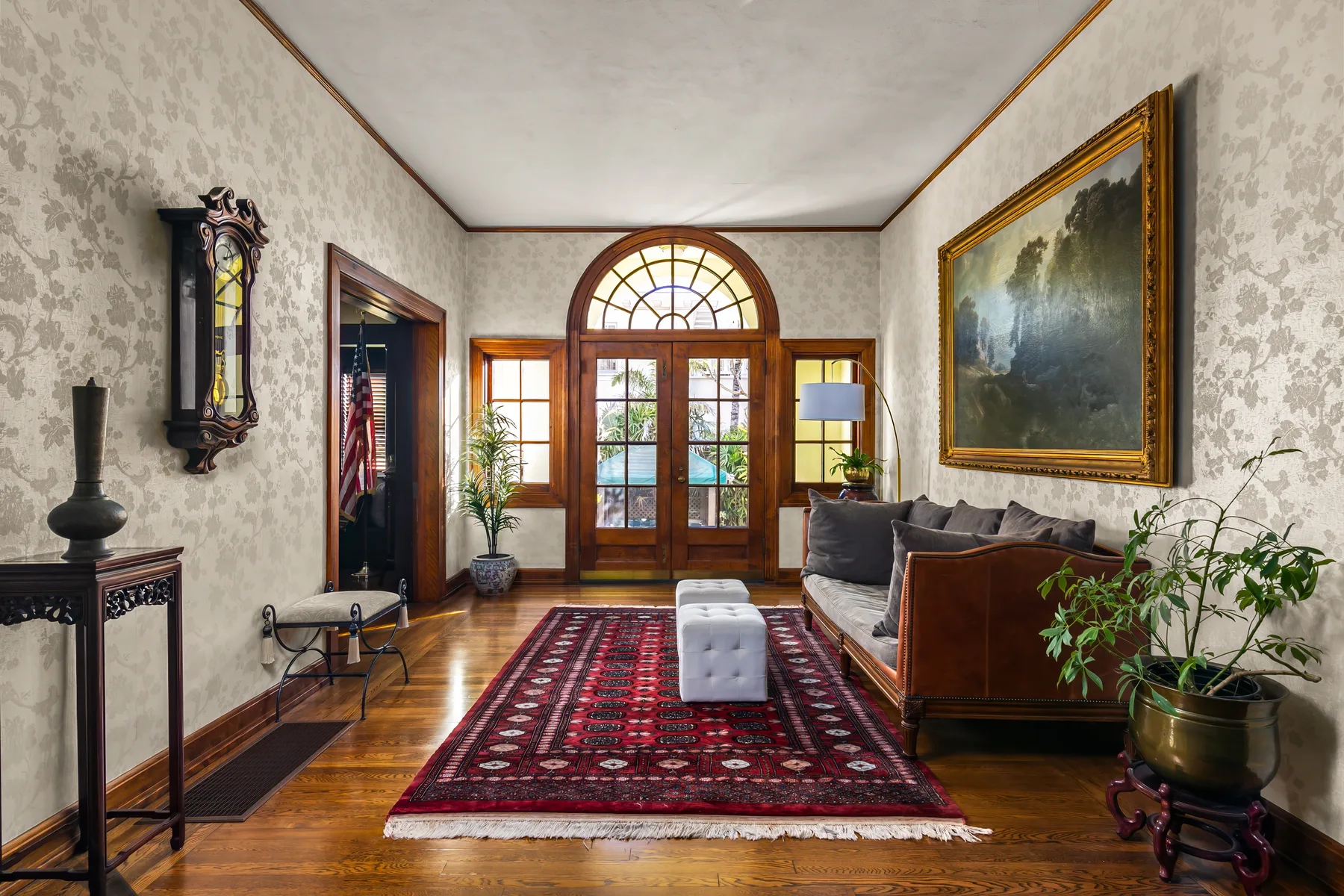 A traditional living room with a patterned rug, seating, and an arched glass doorway.