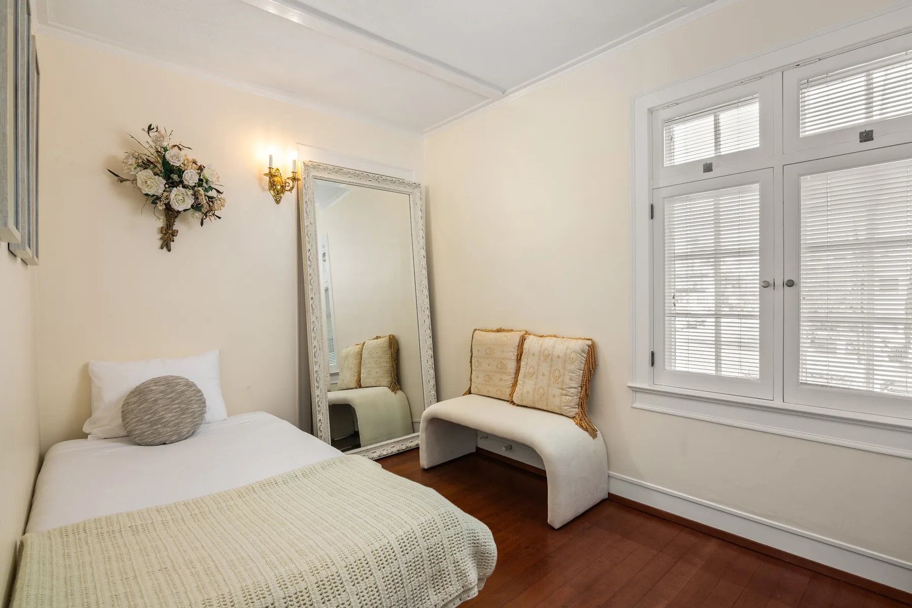 A bright bedroom with a bed, a cushioned bench, and a large window.