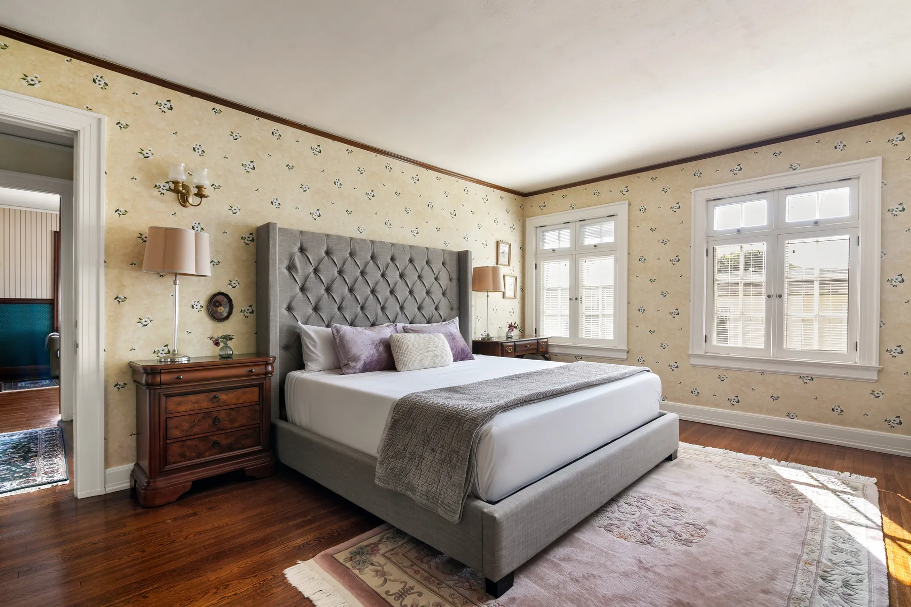 A bedroom with a large bed, bedside tables, and several windows.