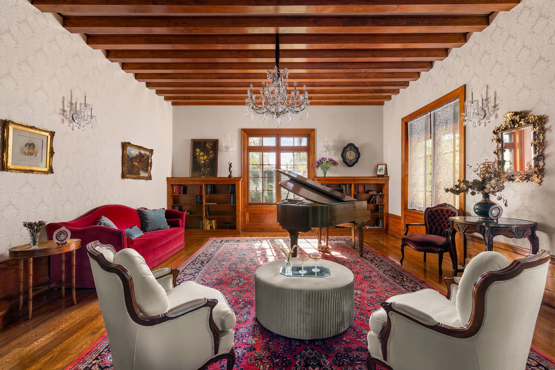 A living room with a grand piano, red seating, and a patterned rug.
