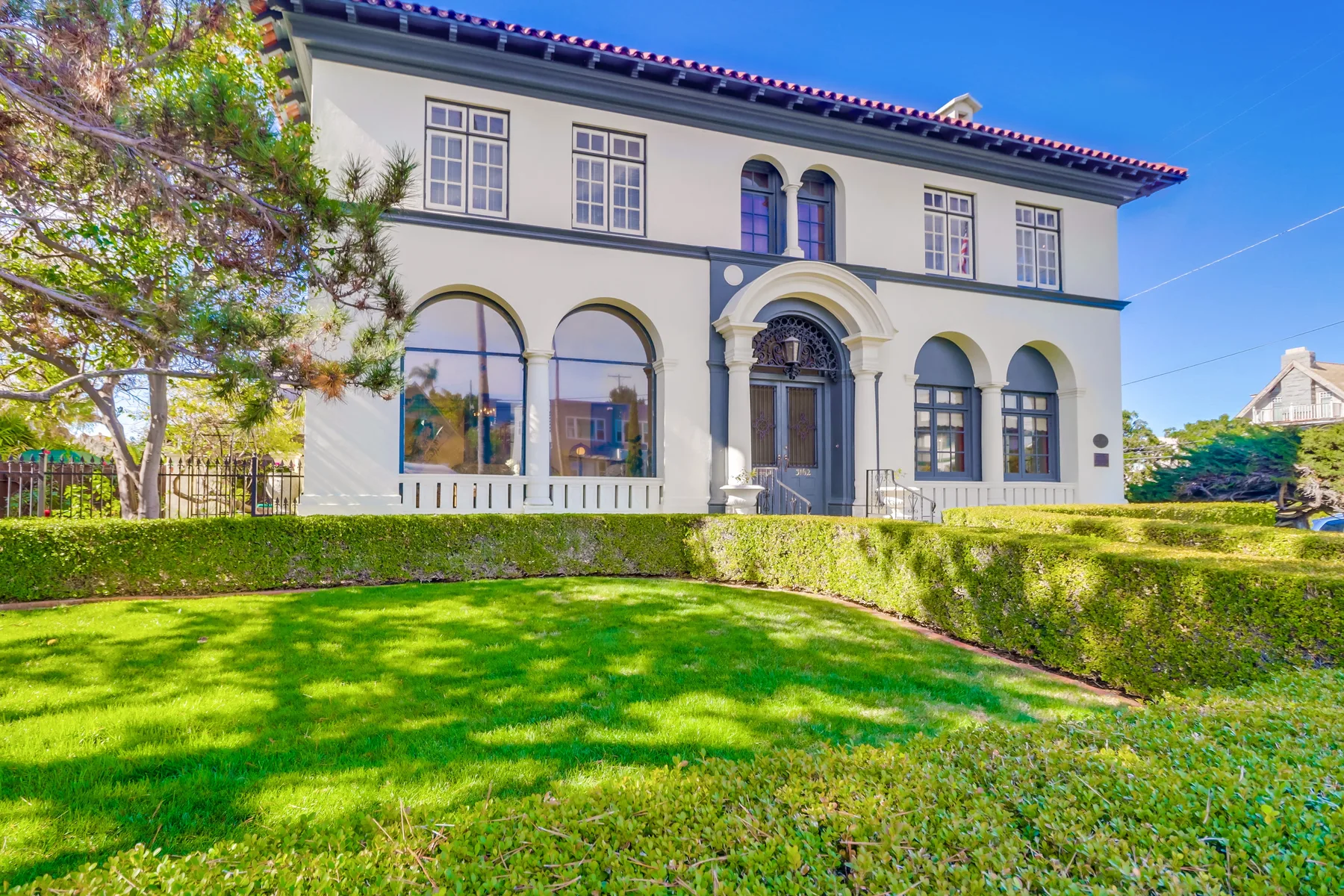 A large white house stands behind a green lawn and trimmed hedges.