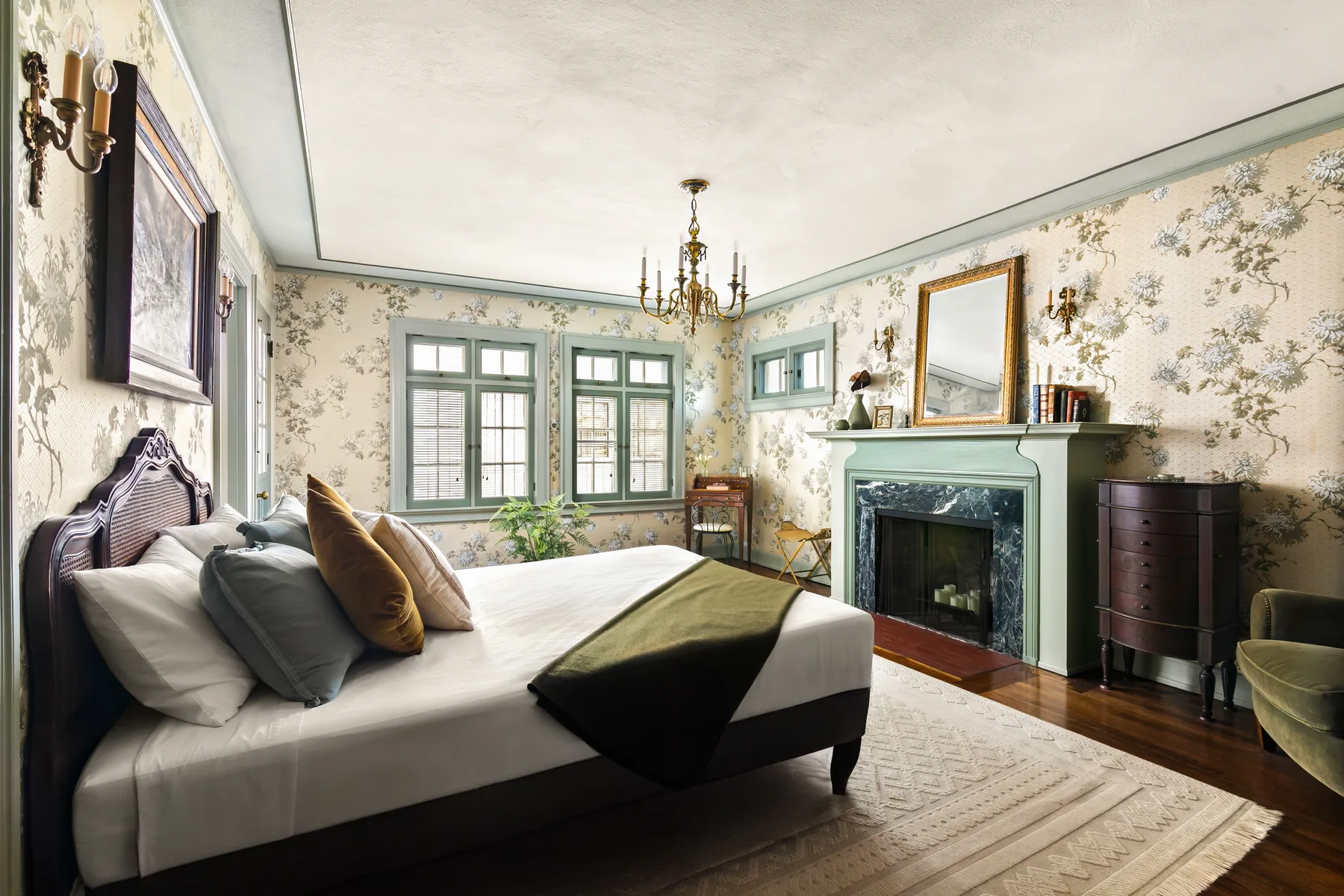 A bedroom with a bed, patterned wallpaper, and a fireplace.