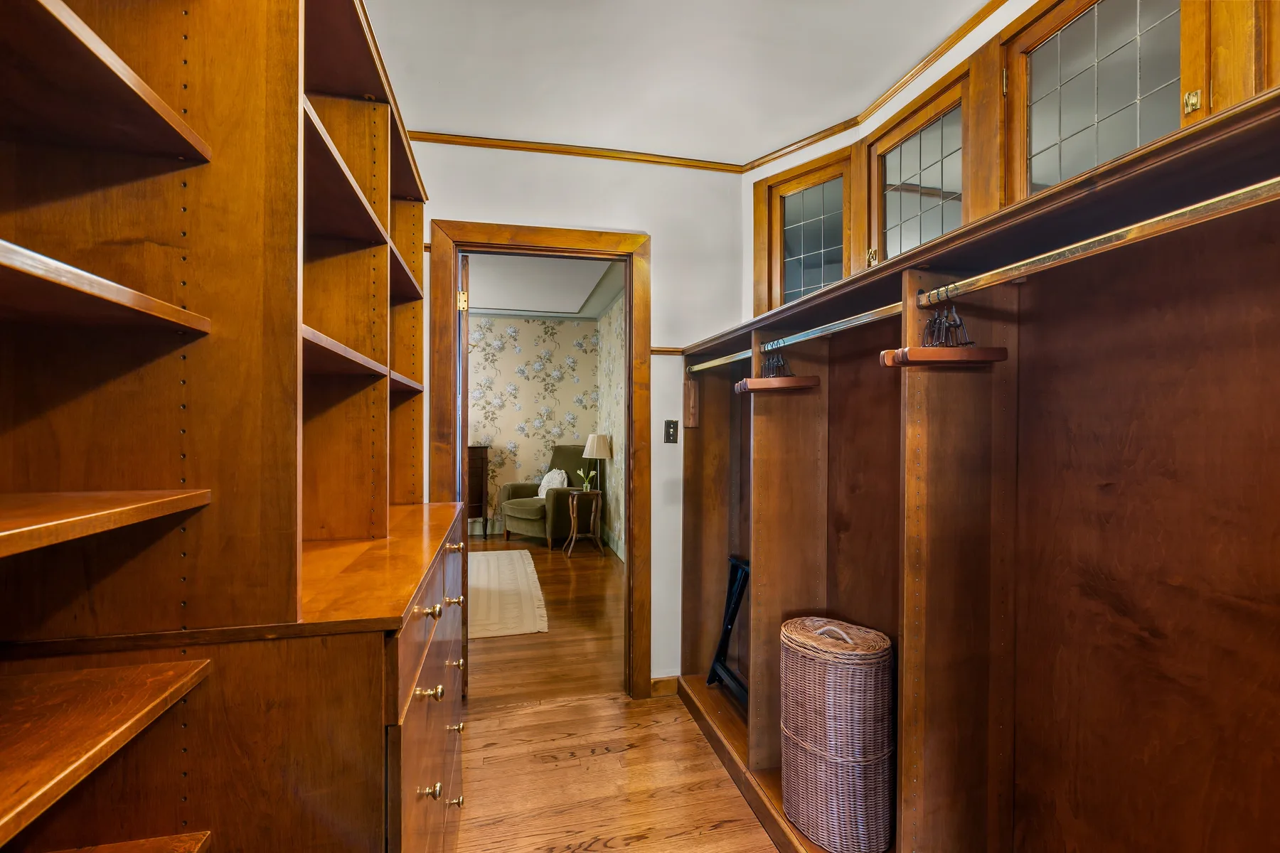 A wood-paneled dressing room has open shelving and a view into an adjoining room.