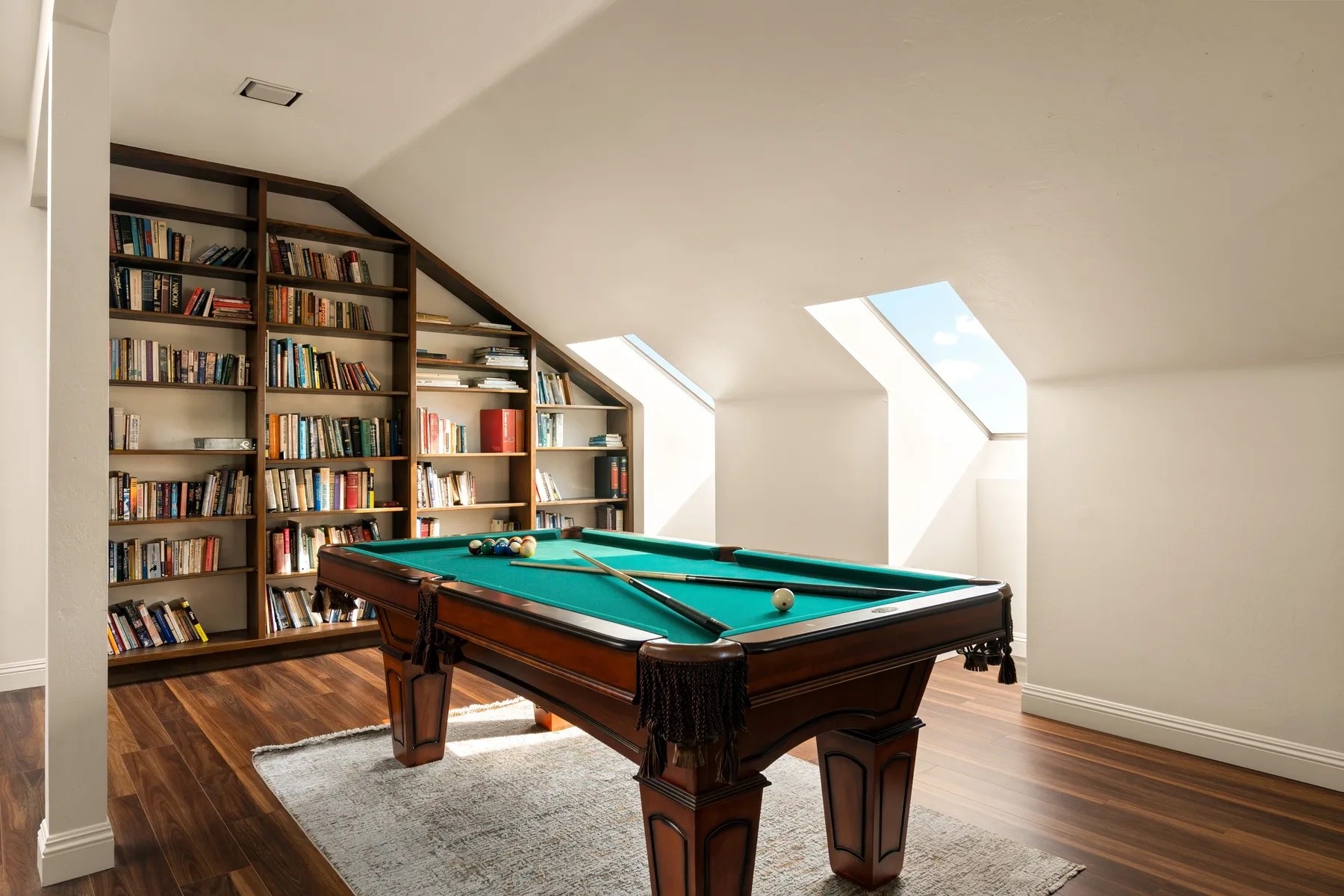 A billiards table sits in a bright attic room lined with bookshelves.
