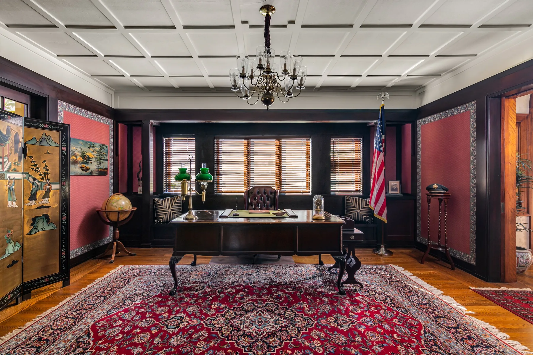 A traditional office with a desk centered on a patterned rug beneath a chandelier.