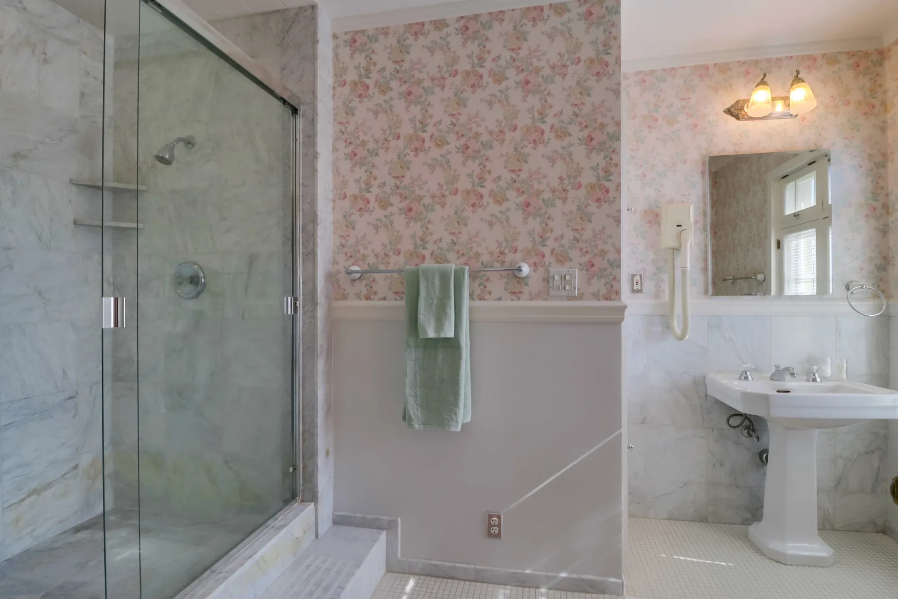 A bathroom with a glass shower, sink, and floral wallpaper.