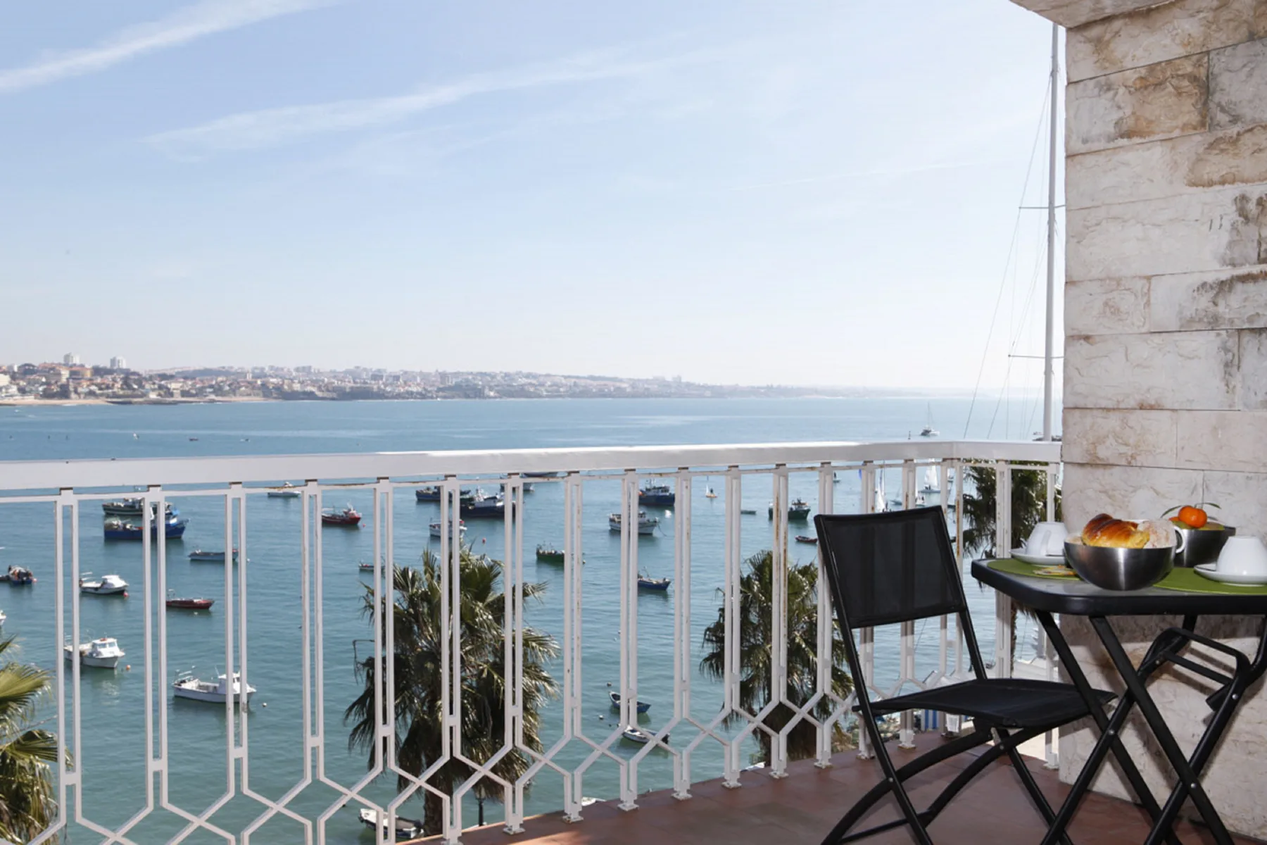 A balcony seating area overlooks the bay, with boats visible on the water.