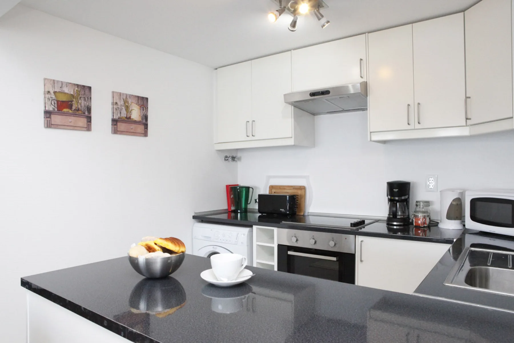 A bright kitchen with white cabinets, dark countertops, and a sink.