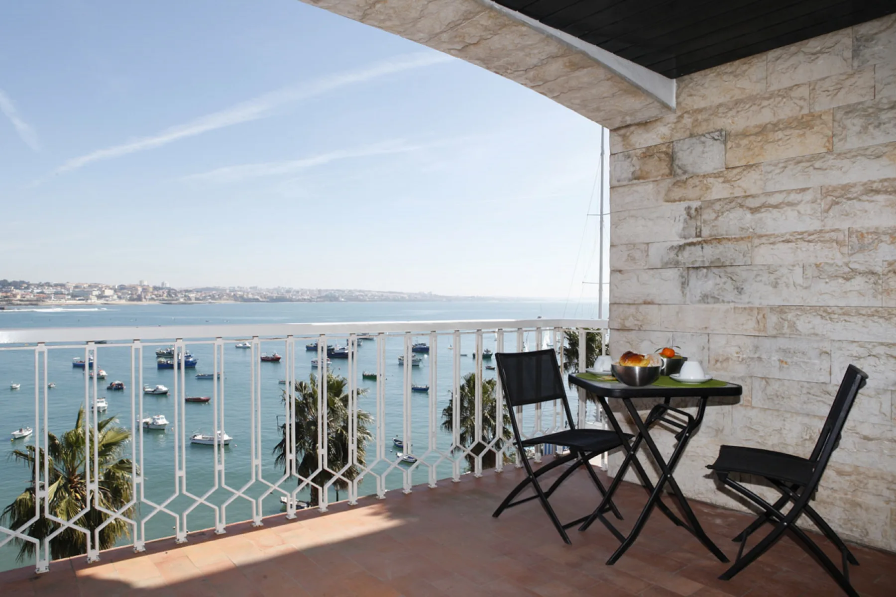 A balcony dining area overlooks the bay, with boats visible on the water.