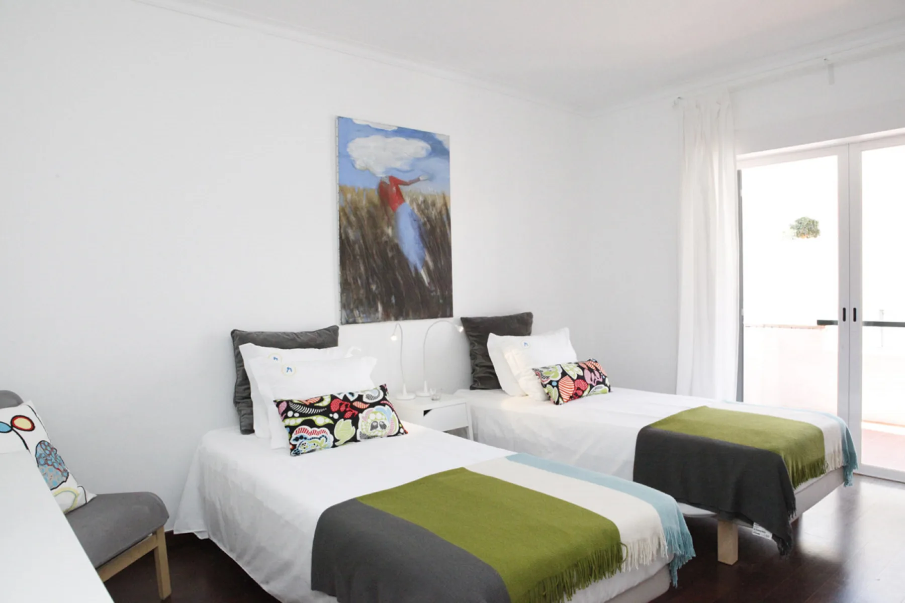 A bright bedroom with two beds and colorful artwork above them.