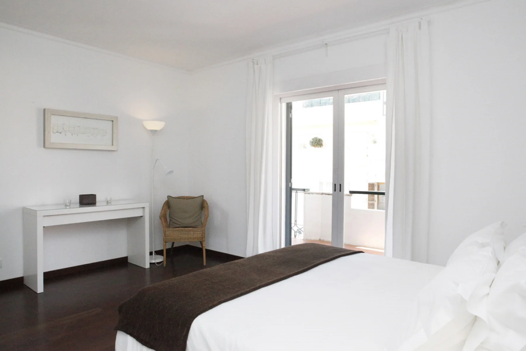 A bright bedroom with a bed, desk, and doors opening onto a balcony.