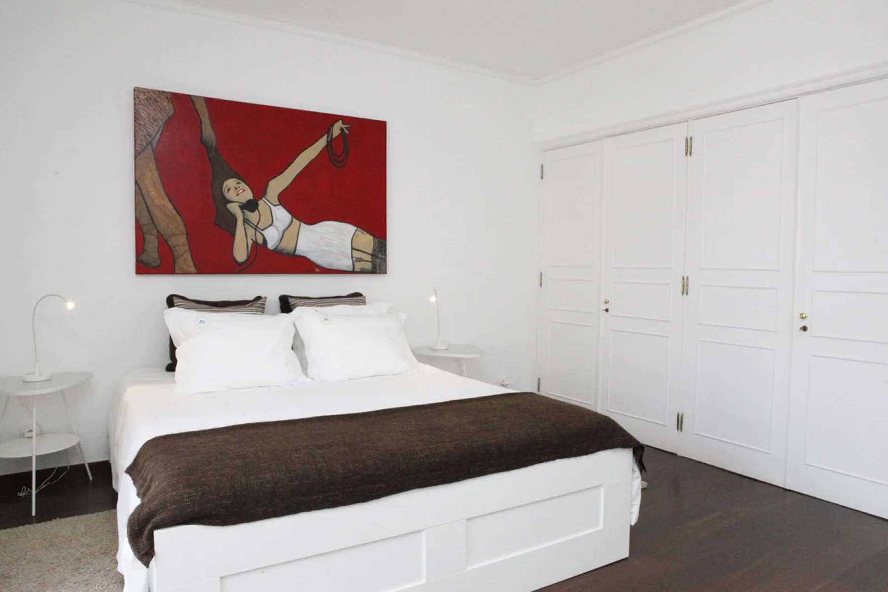 A bedroom with a bed, bedside tables, and colorful artwork above the headboard.