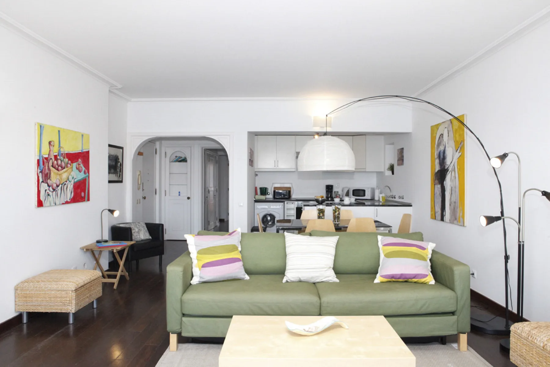 A bright living room with green seating and an open kitchen behind it.