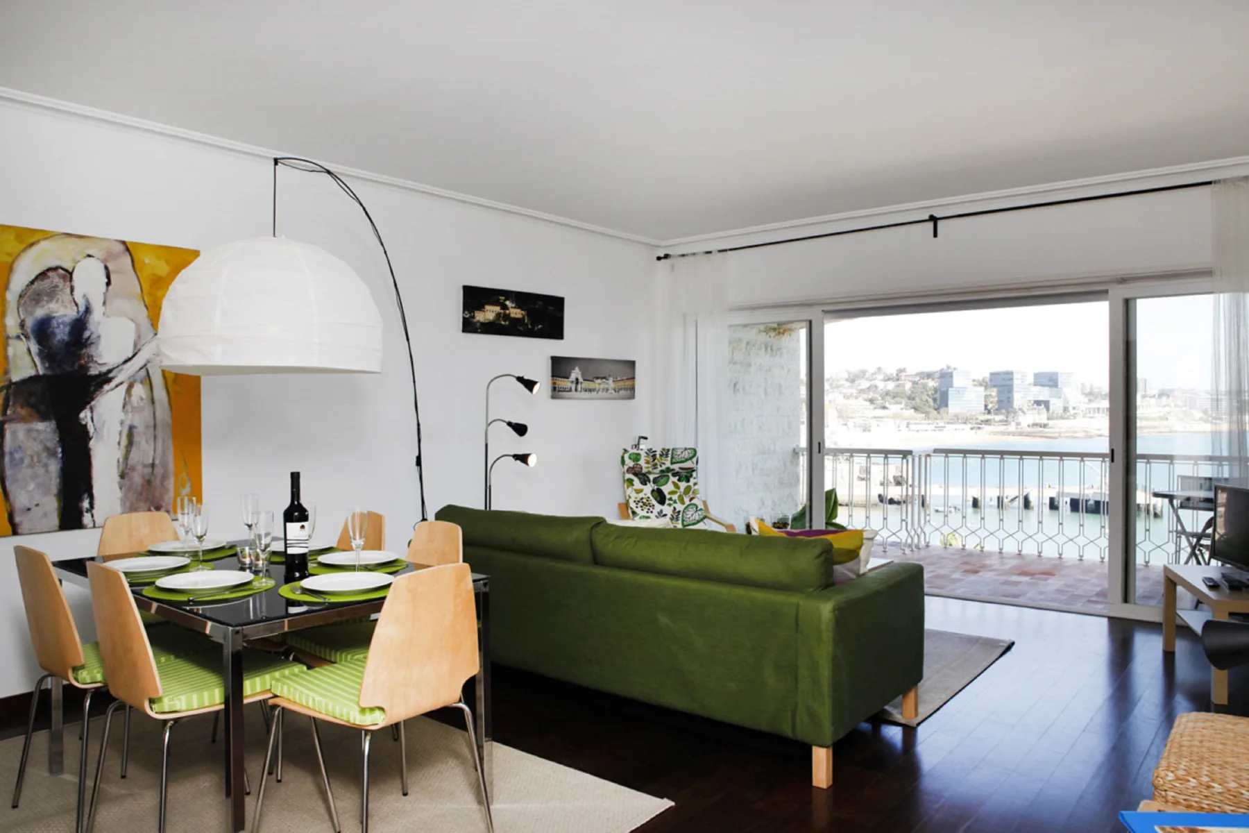 A living and dining area opens onto a balcony with a view of the water.