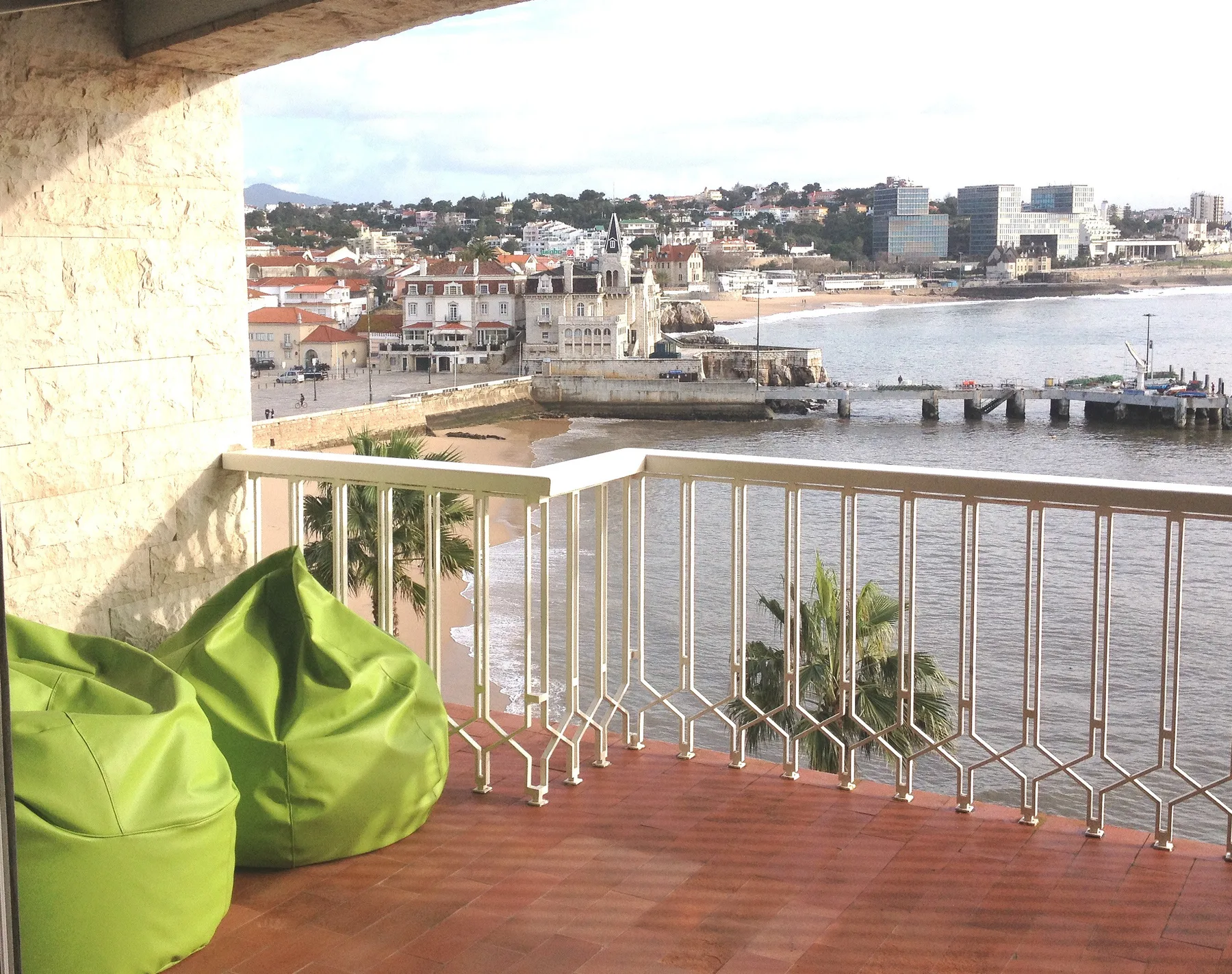 Un balcón da a la bahía y a edificios junto al agua, con asientos verdes en primer plano.