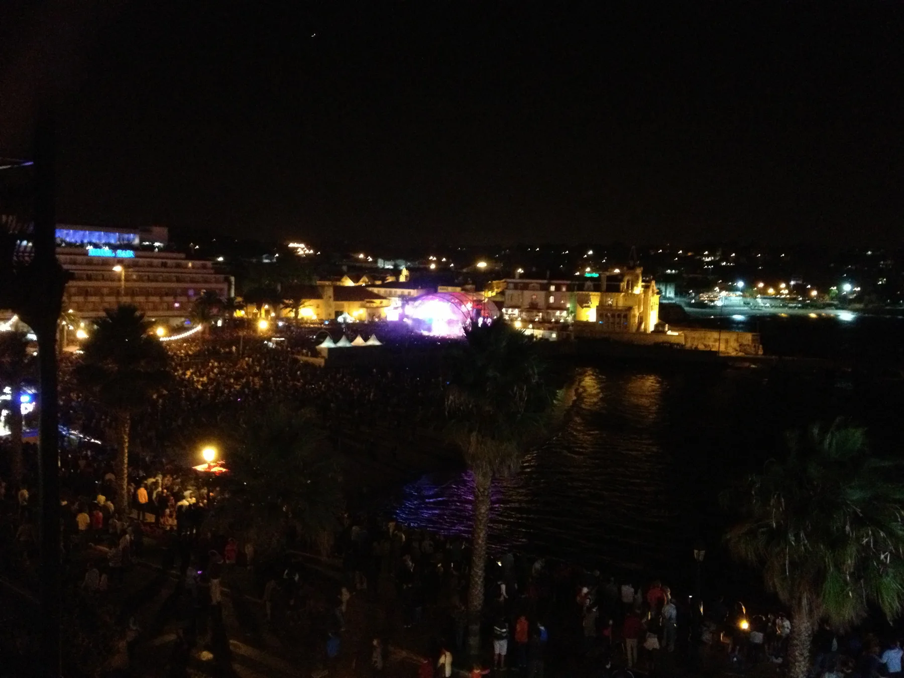 Nighttime waterfront view with illuminated buildings and lights along the shore.