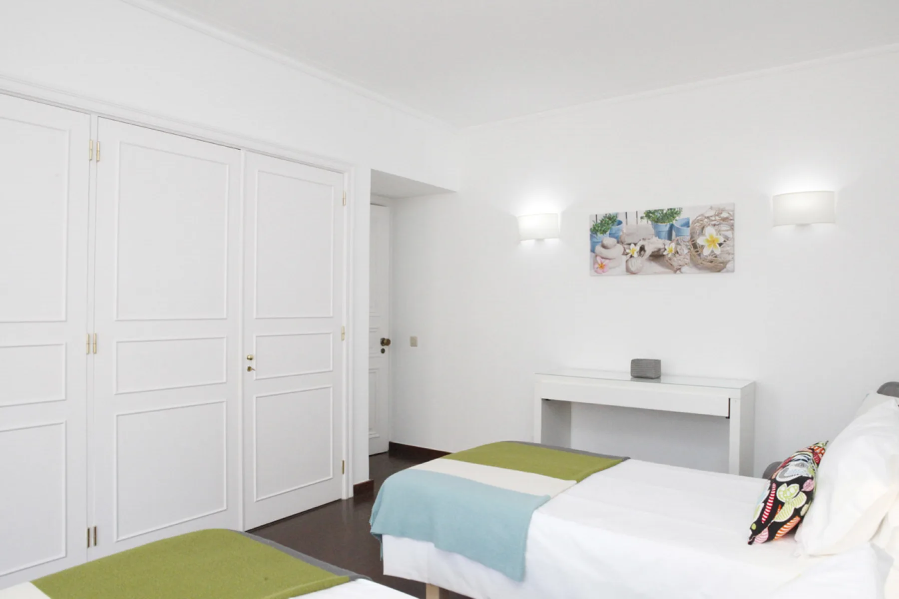 A bright bedroom with a bed, white paneled wardrobes, and a small wall painting.
