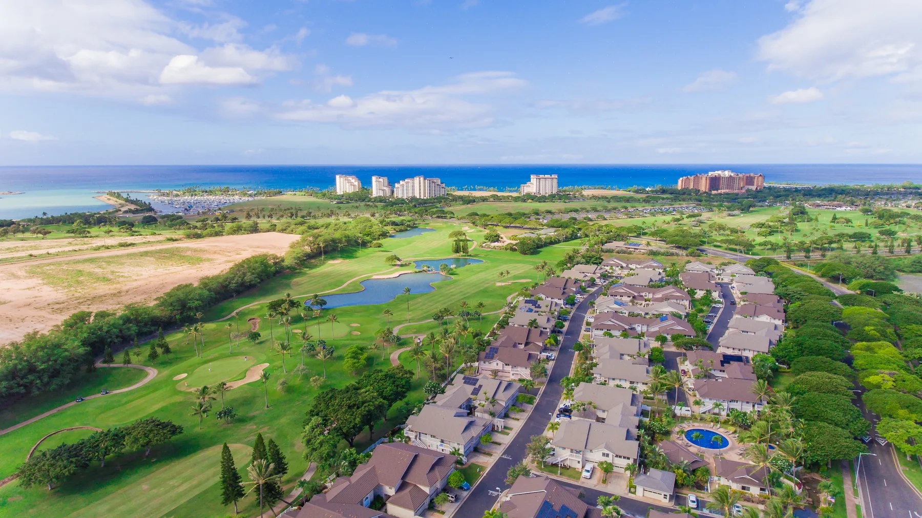 Una vista aérea muestra un campo de golf costero junto a edificios residenciales y el océano.