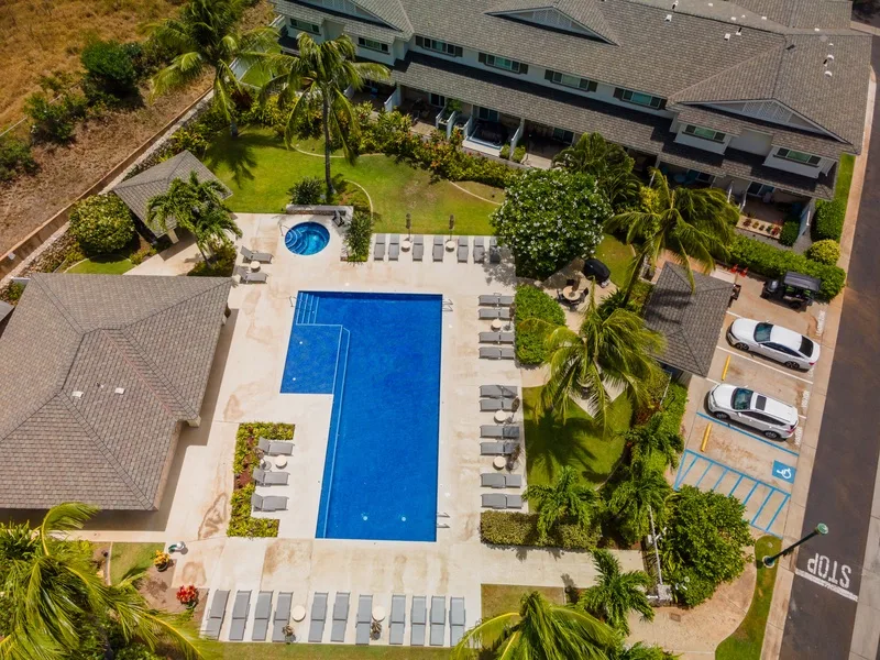 Vista aérea de un patio con piscina, tumbonas y palmeras.