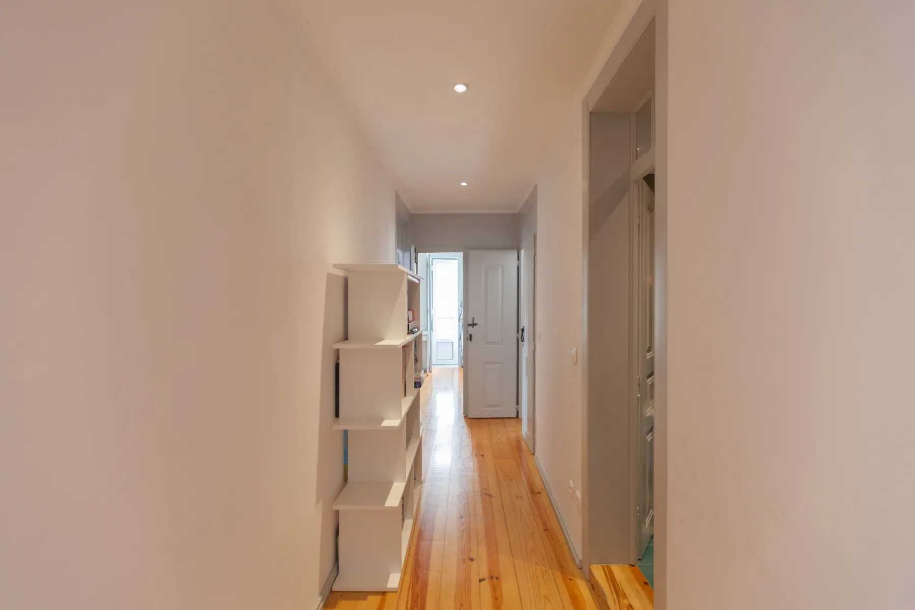 A narrow hallway with wooden flooring and built-in shelving.