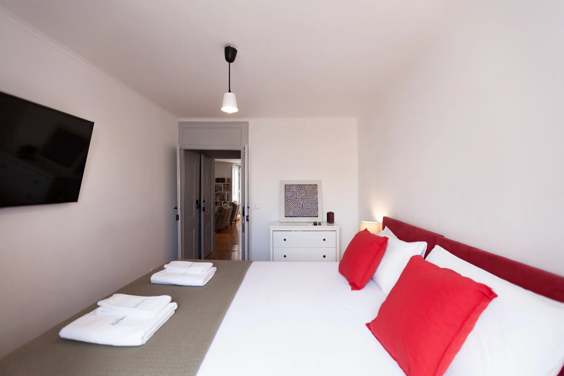 A bright bedroom with a bed dressed in white and red linens.