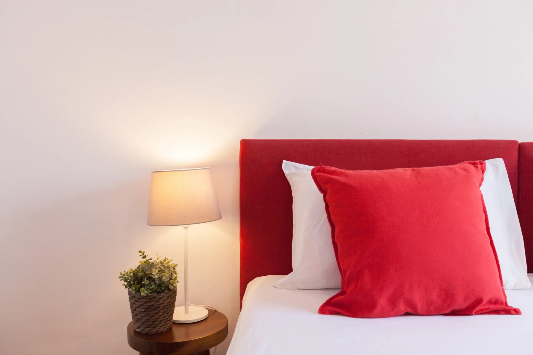 A bedroom with a red headboard, white bedding, and a bedside lamp.