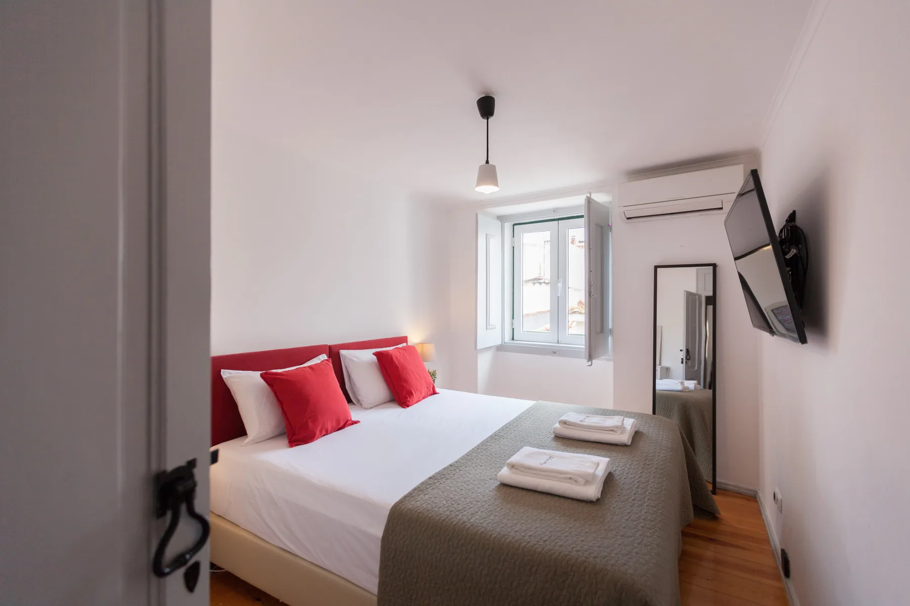 A bright bedroom with a double bed, folded towels, and a window.