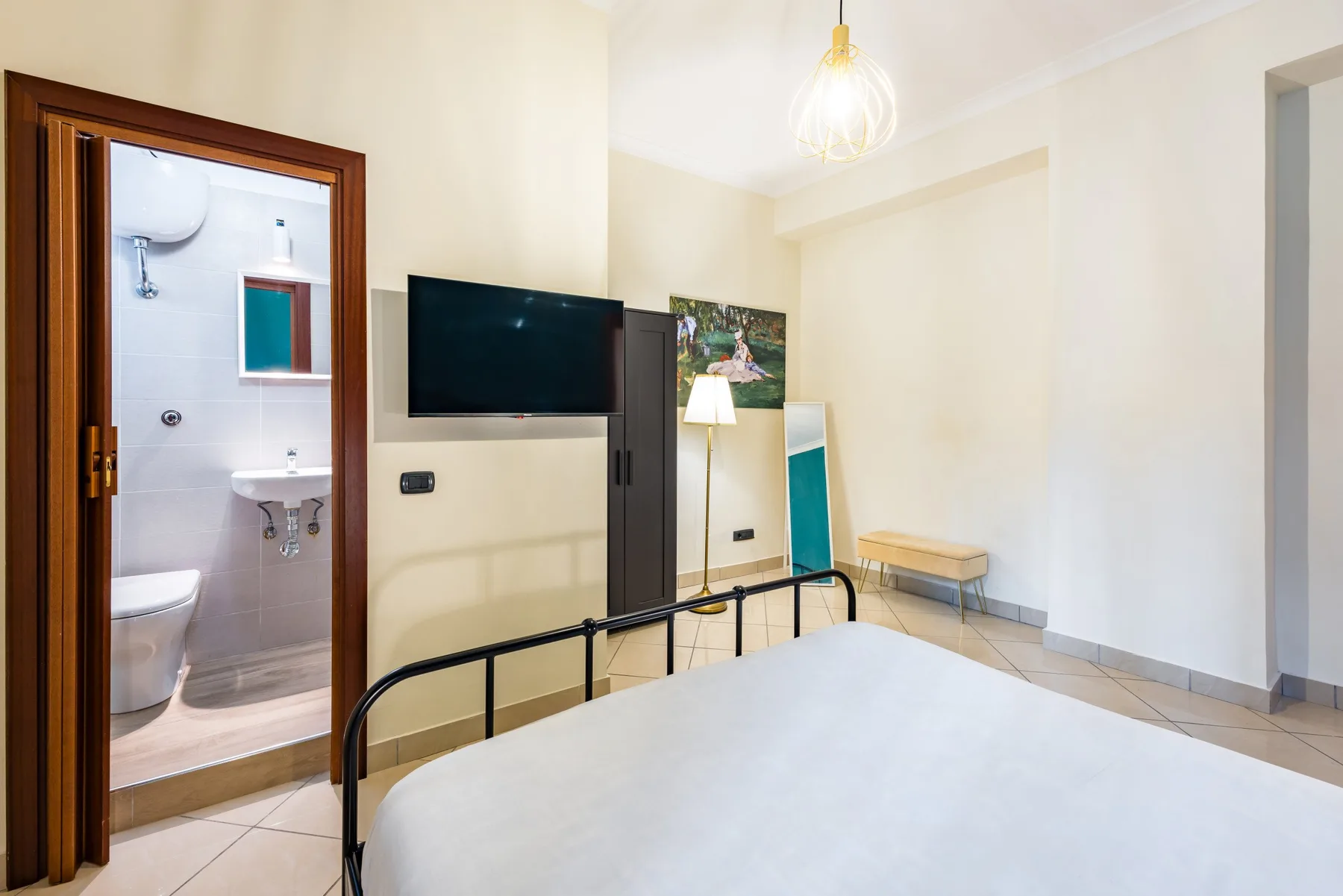 Un dormitorio con cama, televisor en la pared y una puerta abierta al baño.