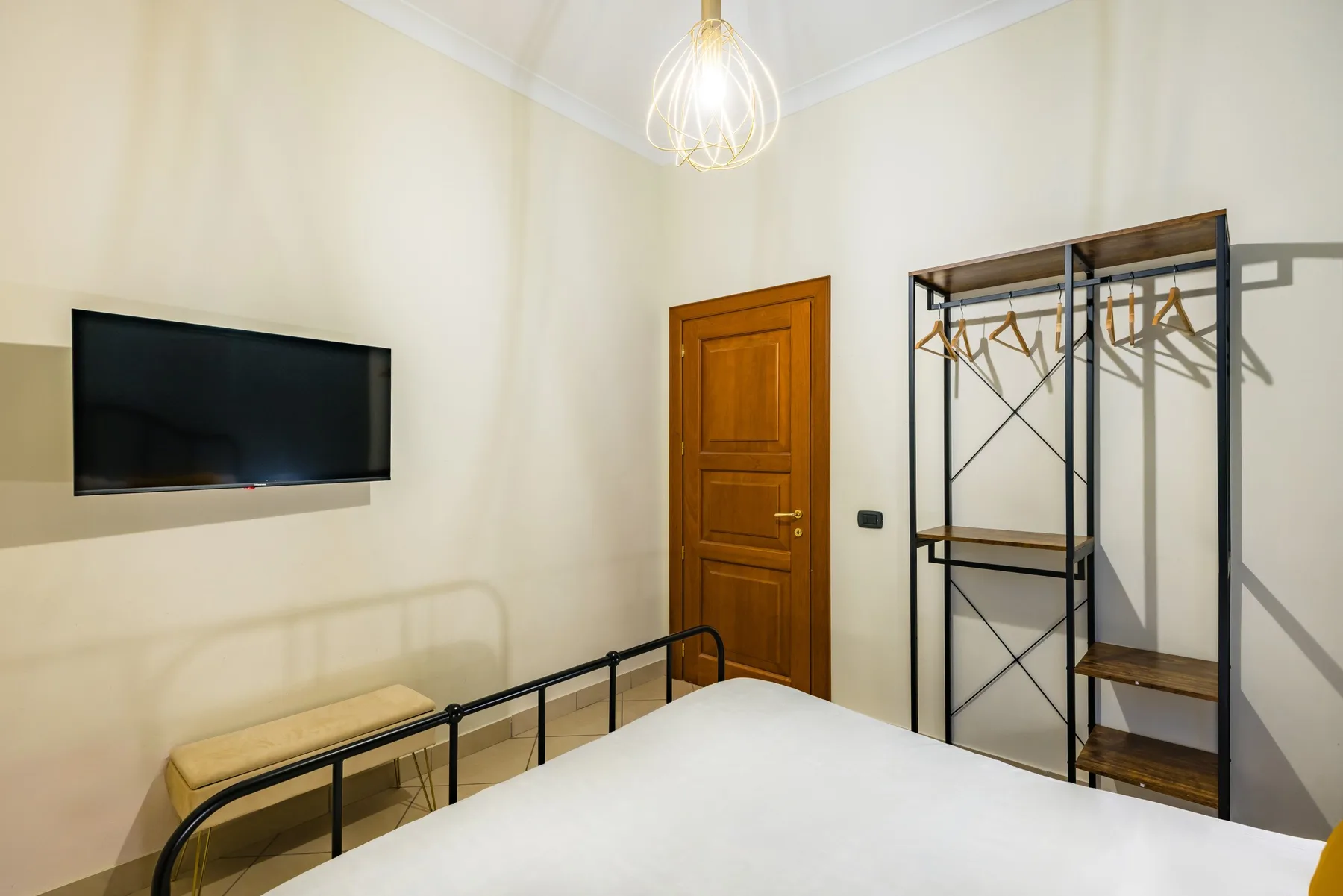 Un dormitorio con cama, televisor montado en la pared y perchero abierto.