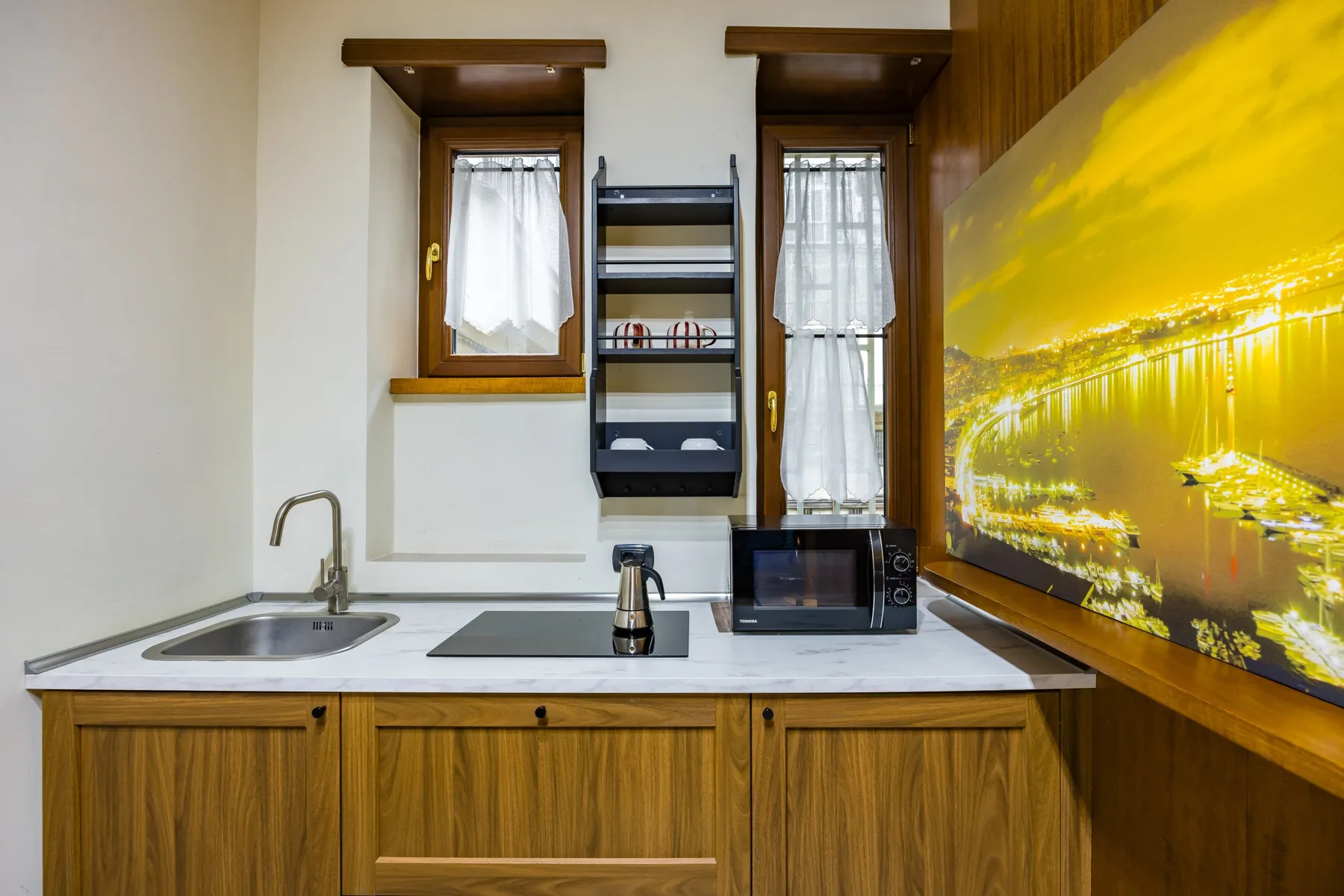 Una cocina compacta tiene armarios de madera, un fregadero y un microondas.