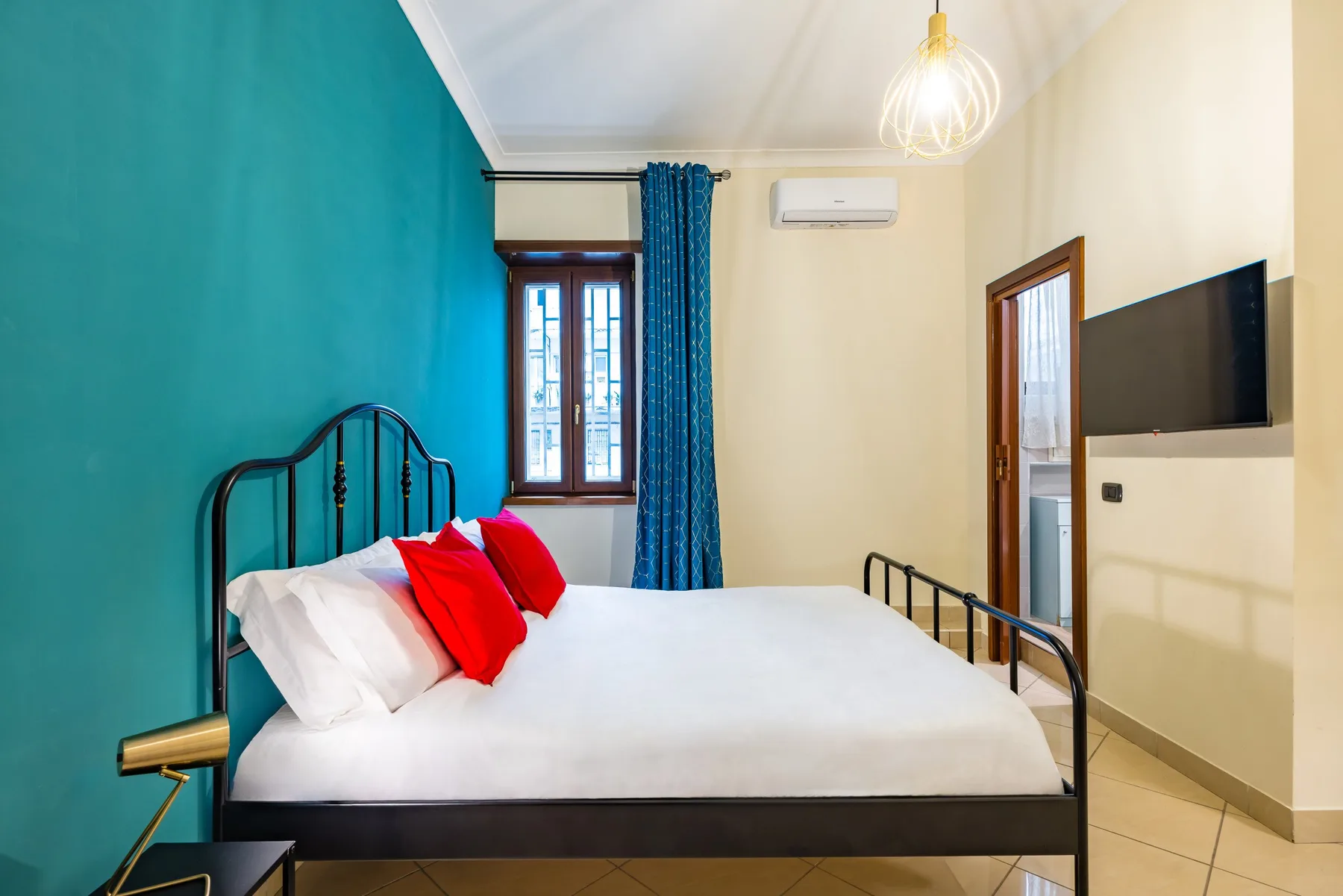 Un dormitorio con cama, pared de acento turquesa y ventana.