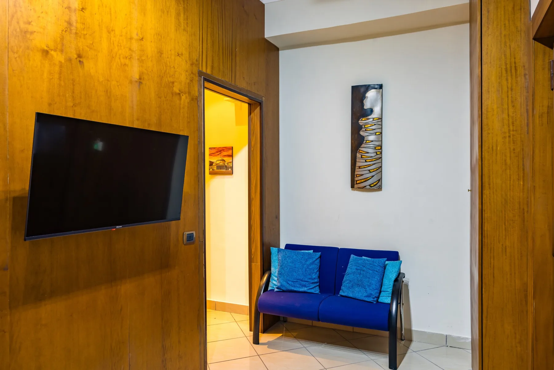 A small blue seating area sits beside a wood-paneled wall and an open doorway.