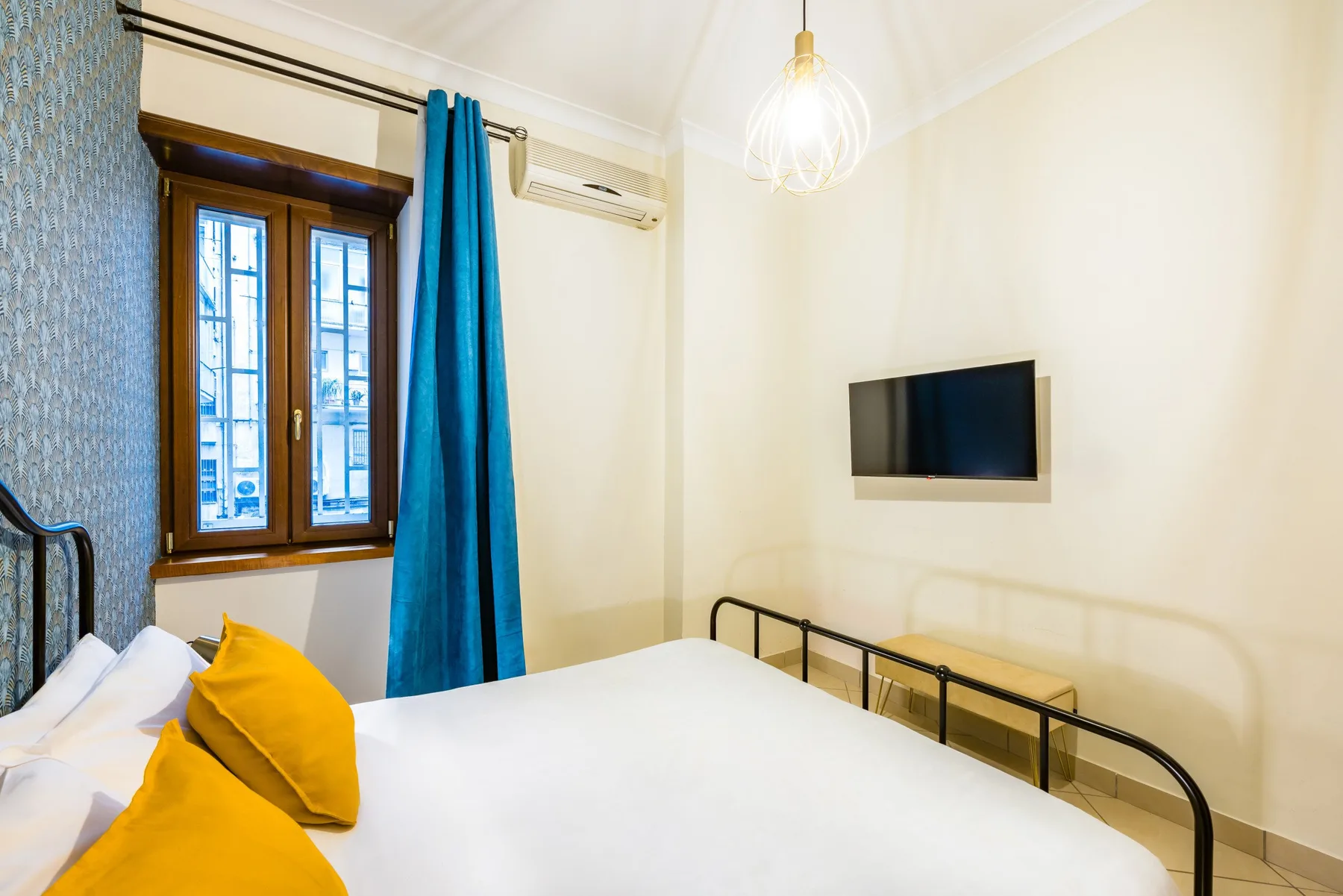 Dormitorio con una cama, una ventana y un televisor en la pared.
