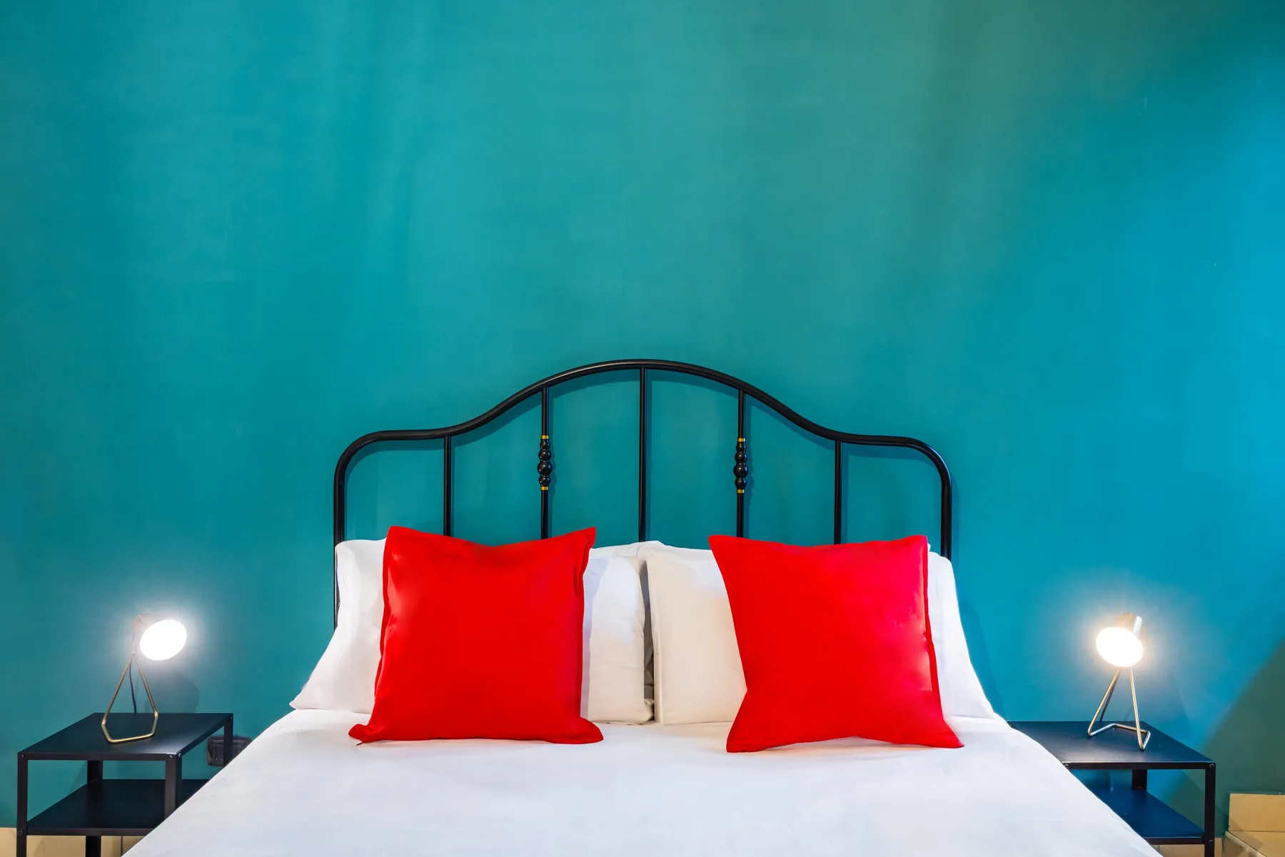 Un dormitorio con una cama, cojines rojos y una pared color turquesa.