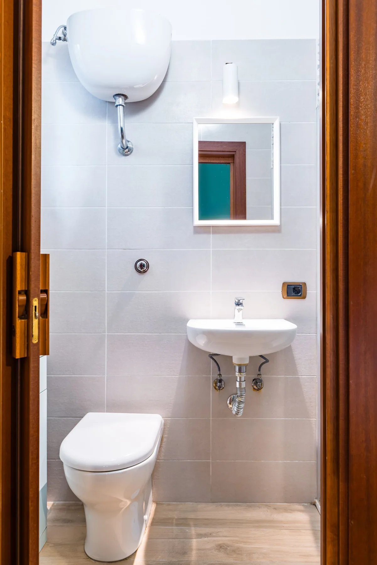 Un baño con azulejos, inodoro, lavabo de pared y espejo.