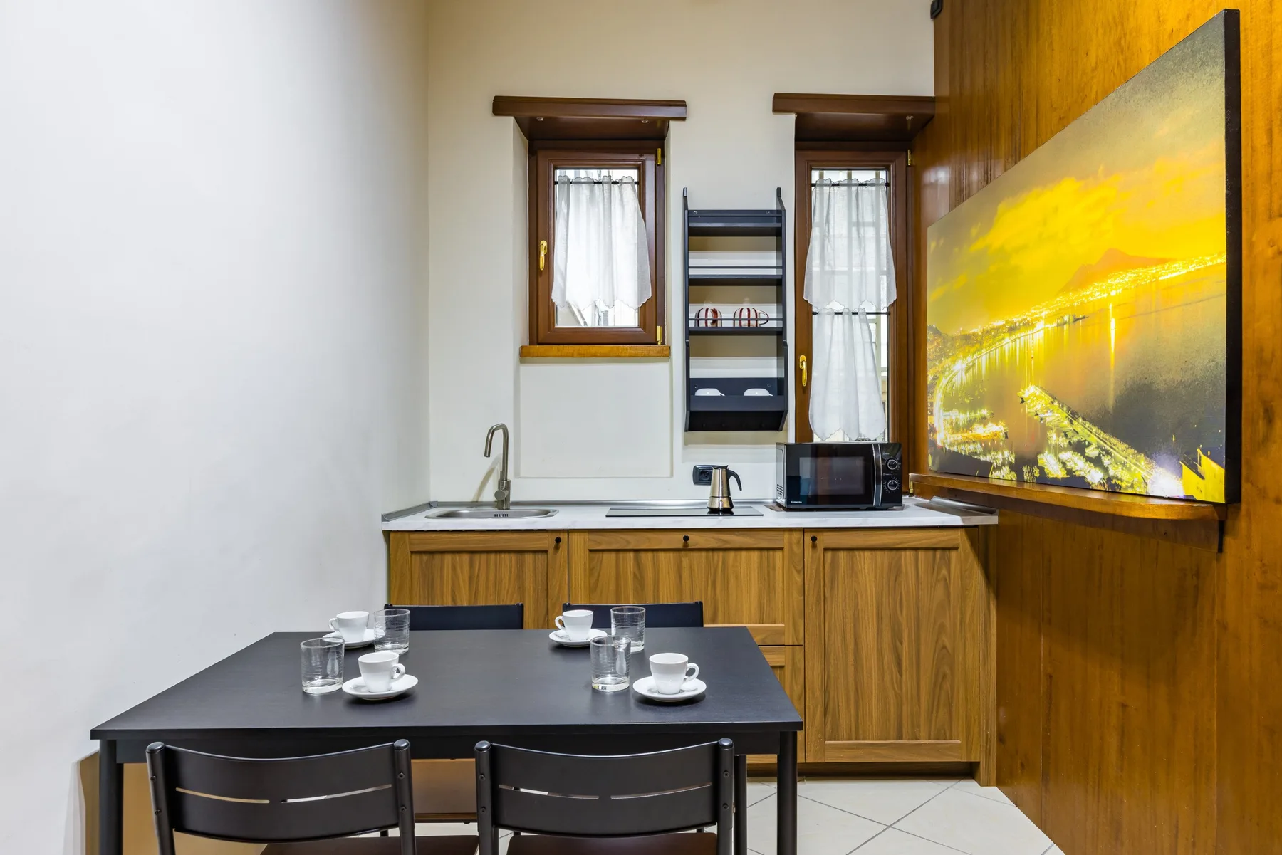 Una pequeña zona de comedor con una mesa frente a una cocina y un cuadro grande en la pared.