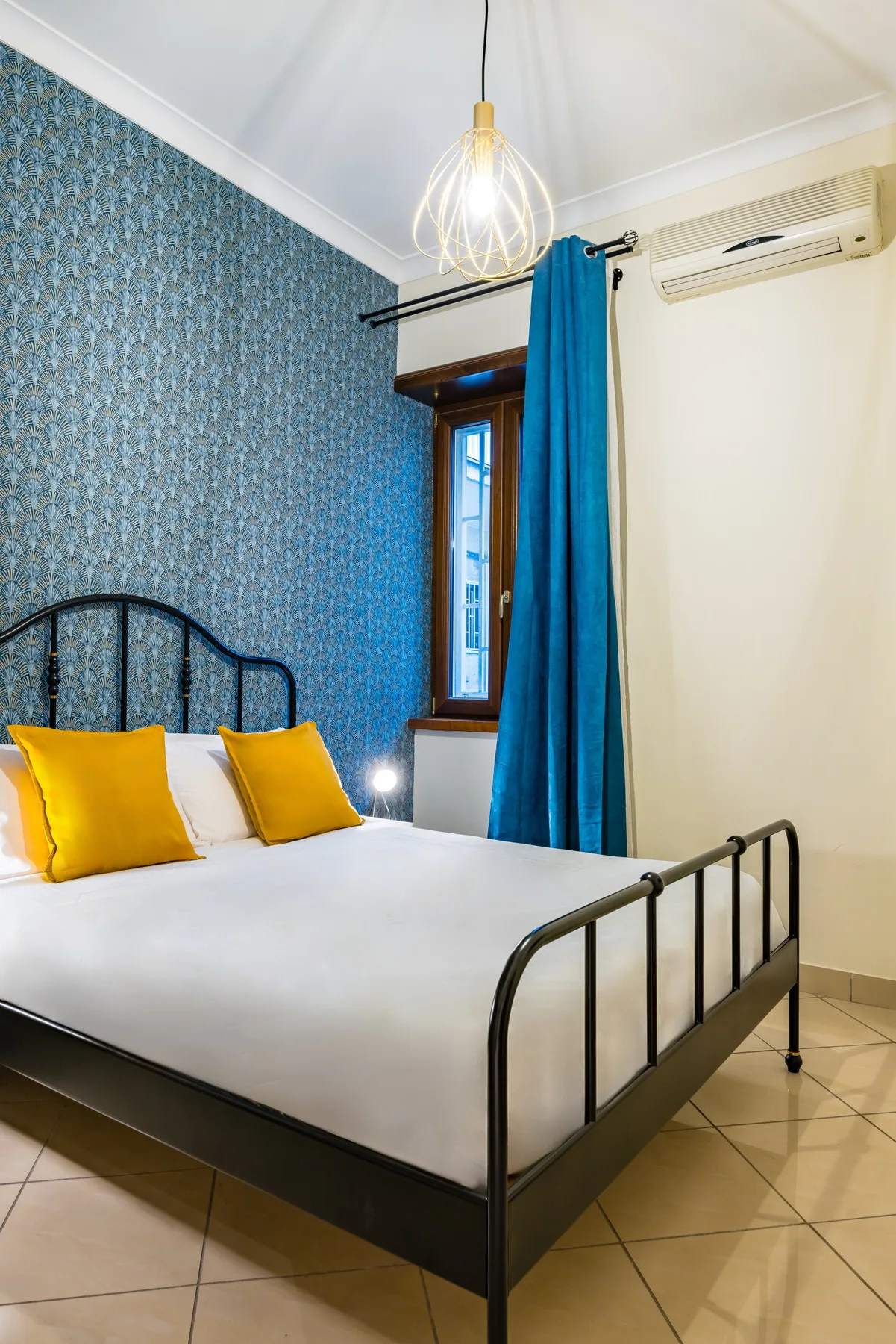 Un dormitorio con una cama de metal negro, almohadas amarillas y una cortina azul.