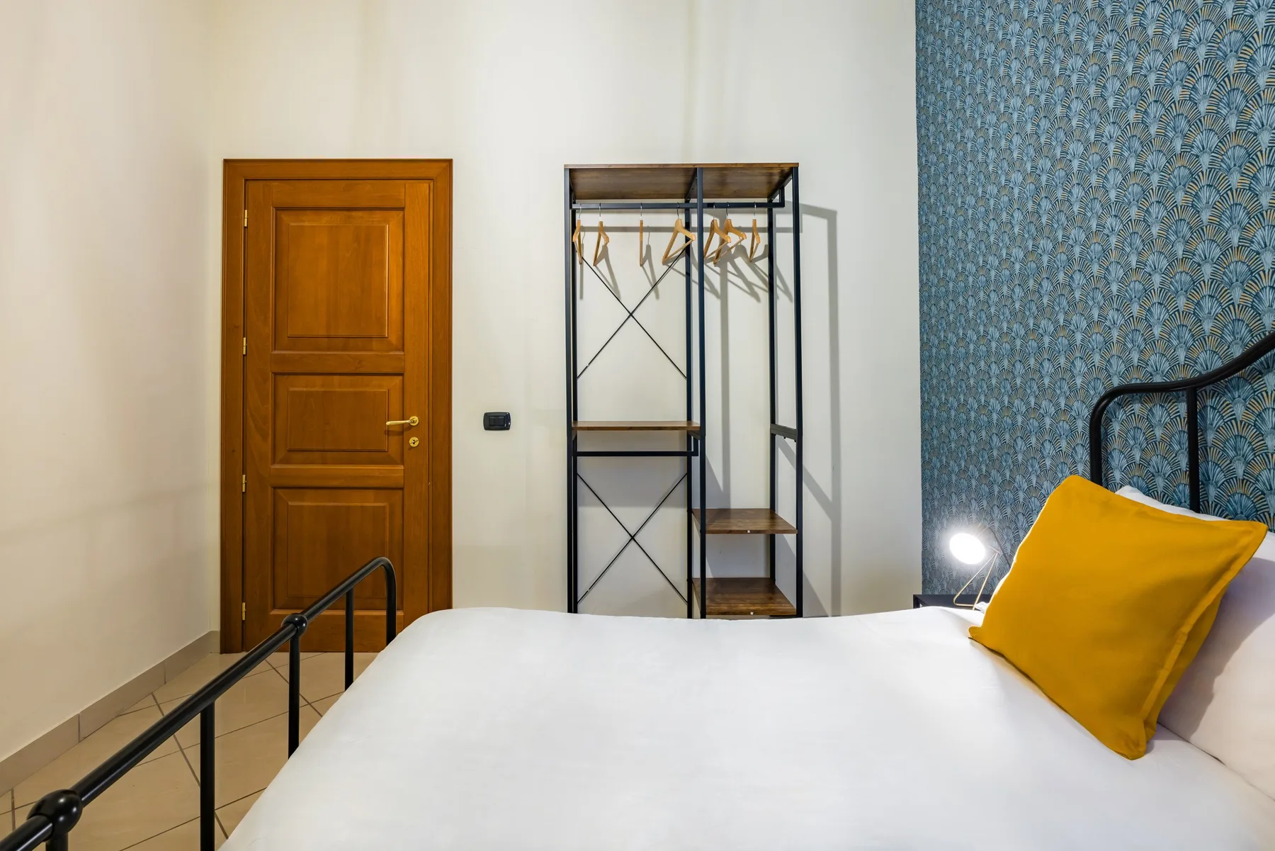 A bedroom with a white bed, yellow cushion, and open clothes rack.
