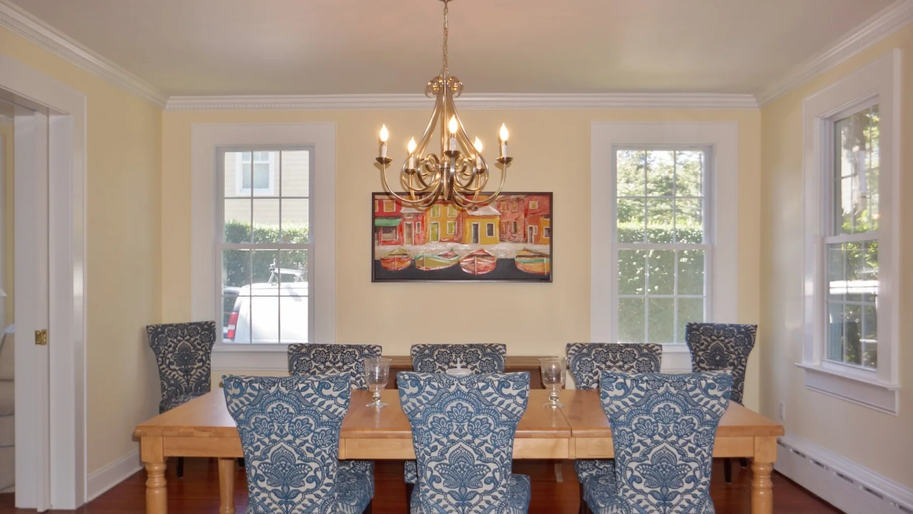 A dining room with a long wooden table, patterned seating, and a hanging chandelier.