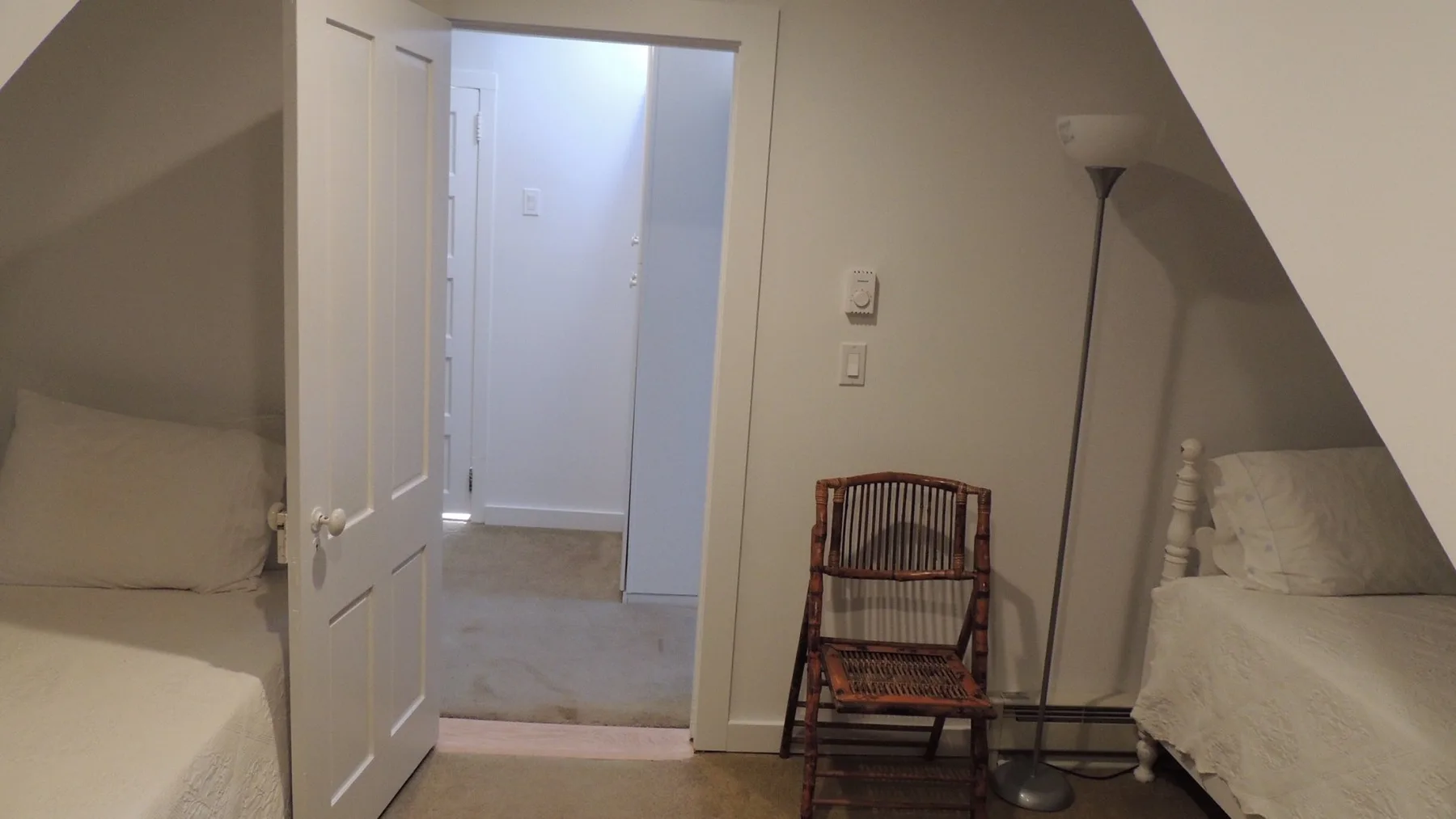 Un dormitorio con una cama, una silla de madera y una lámpara de pie.