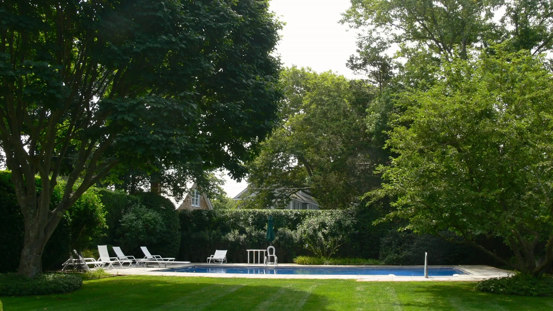 Una piscina al aire libre está junto a un césped verde y árboles frondosos.