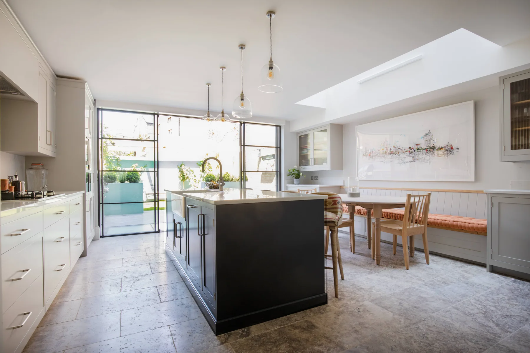 Una cocina y comedor luminosos con una isla central oscura y una mesa de madera.