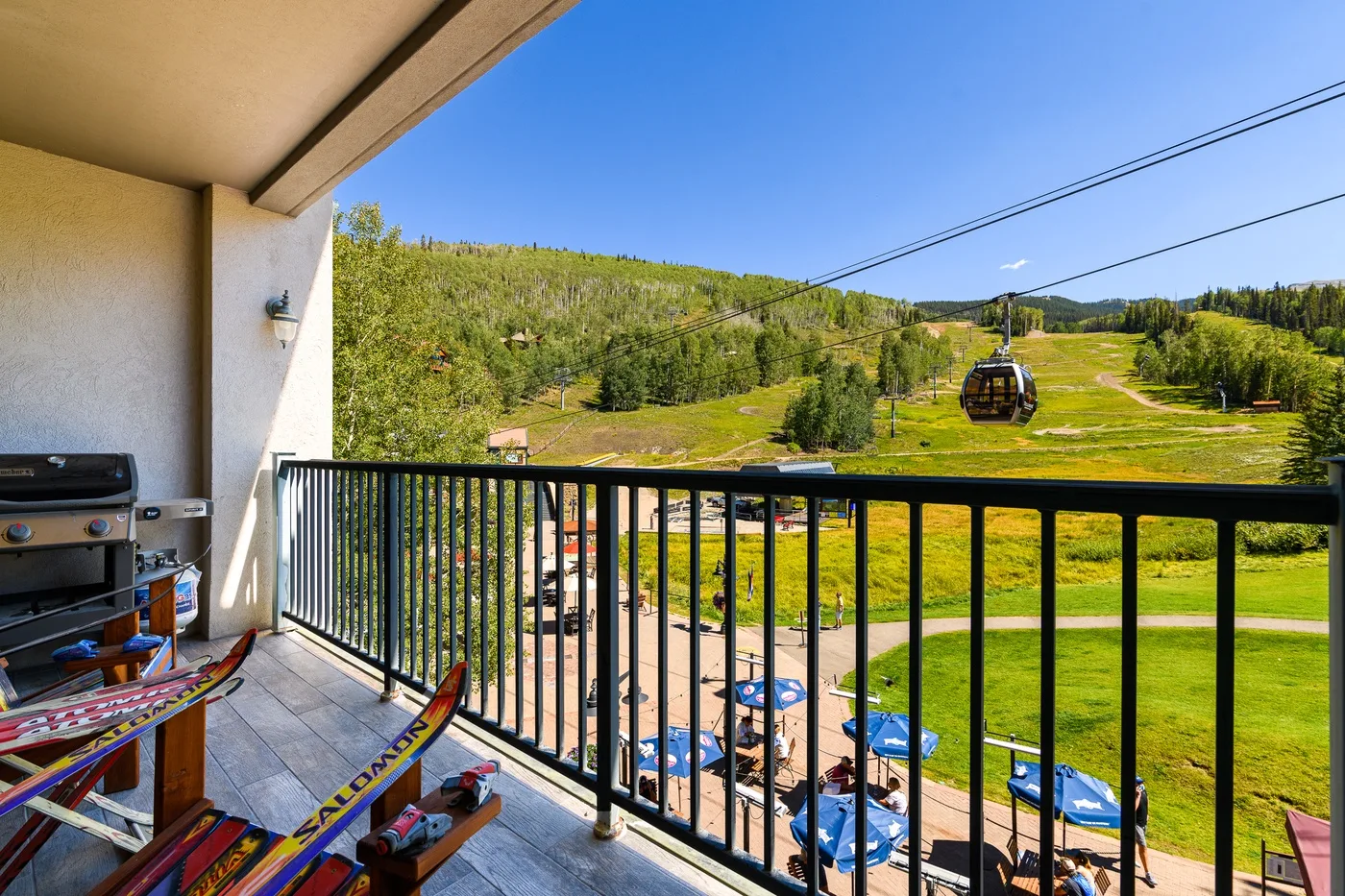 A balcony overlooks a grassy hillside with a gondola and tree-lined slopes.