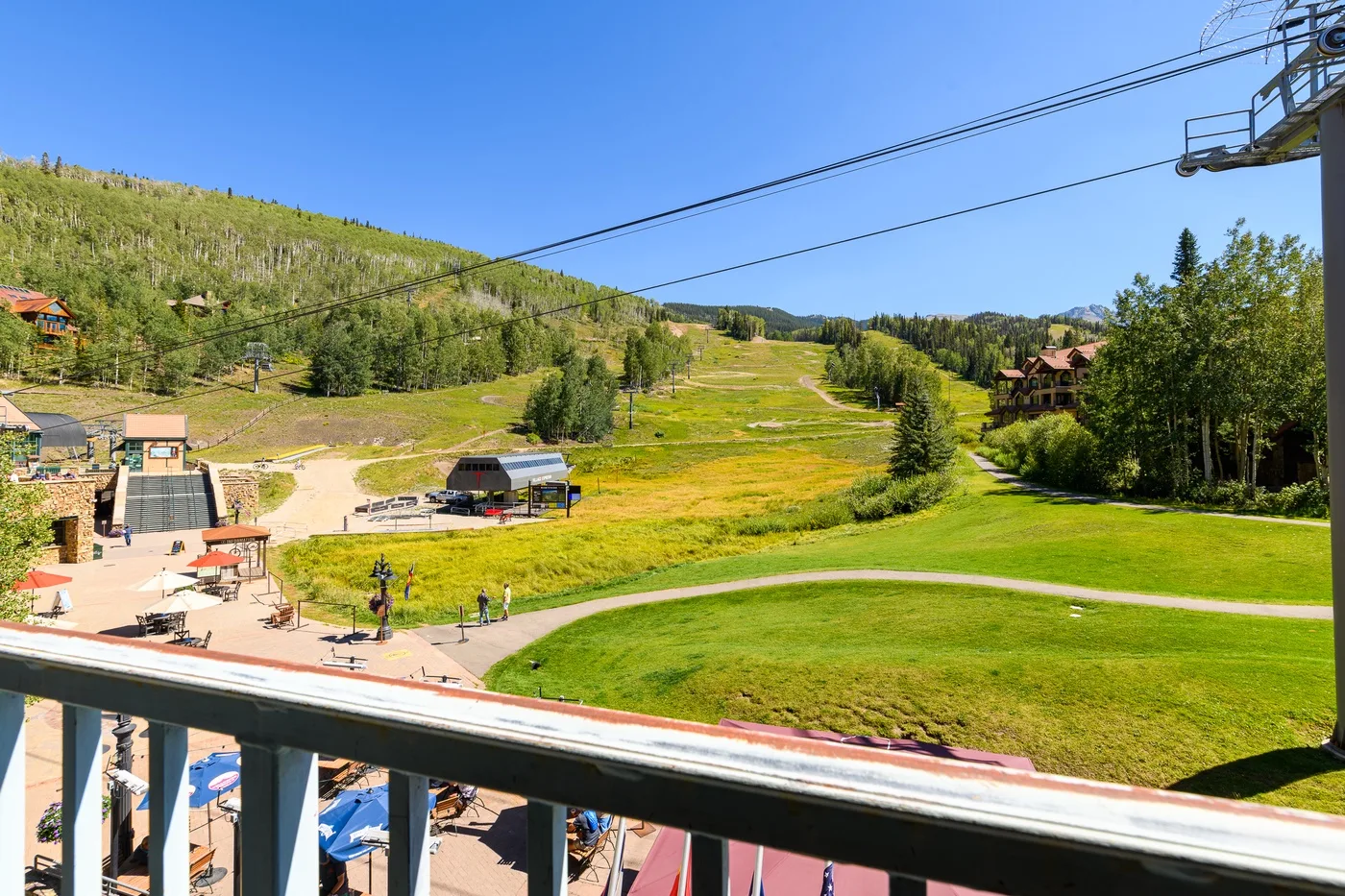 A balcony overlooks a green hillside with walking paths and a mountain lift.